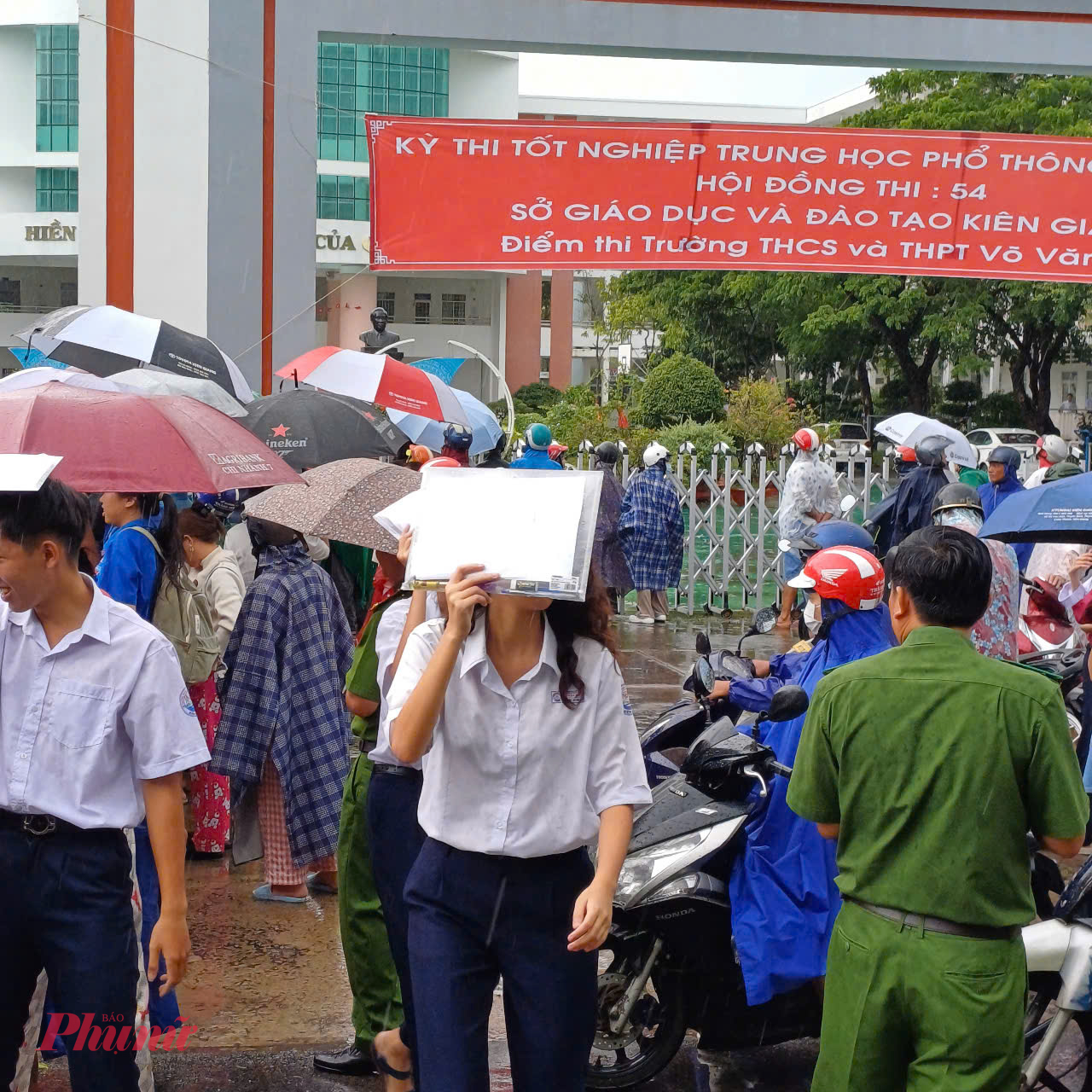 Thi sinh dùng tệp đựng dụng cụ, giấy tờ dự thi che mưa chạy ra với phụ huynh - Ảnh Phú Hữu