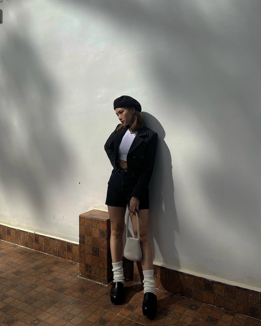 ''Em xinh'' Miu Lê mang đến hình ảnh thanh lịch pha chút phá cách với mũ beret, áo khoác đen và crop top trắng. Cô khéo léo kết hợp quần shorts, vớ cao cổ và giày đế thô, tạo nên tổng thể tối giản nhưng cá tính, vừa cổ điển vừa hiện đại.