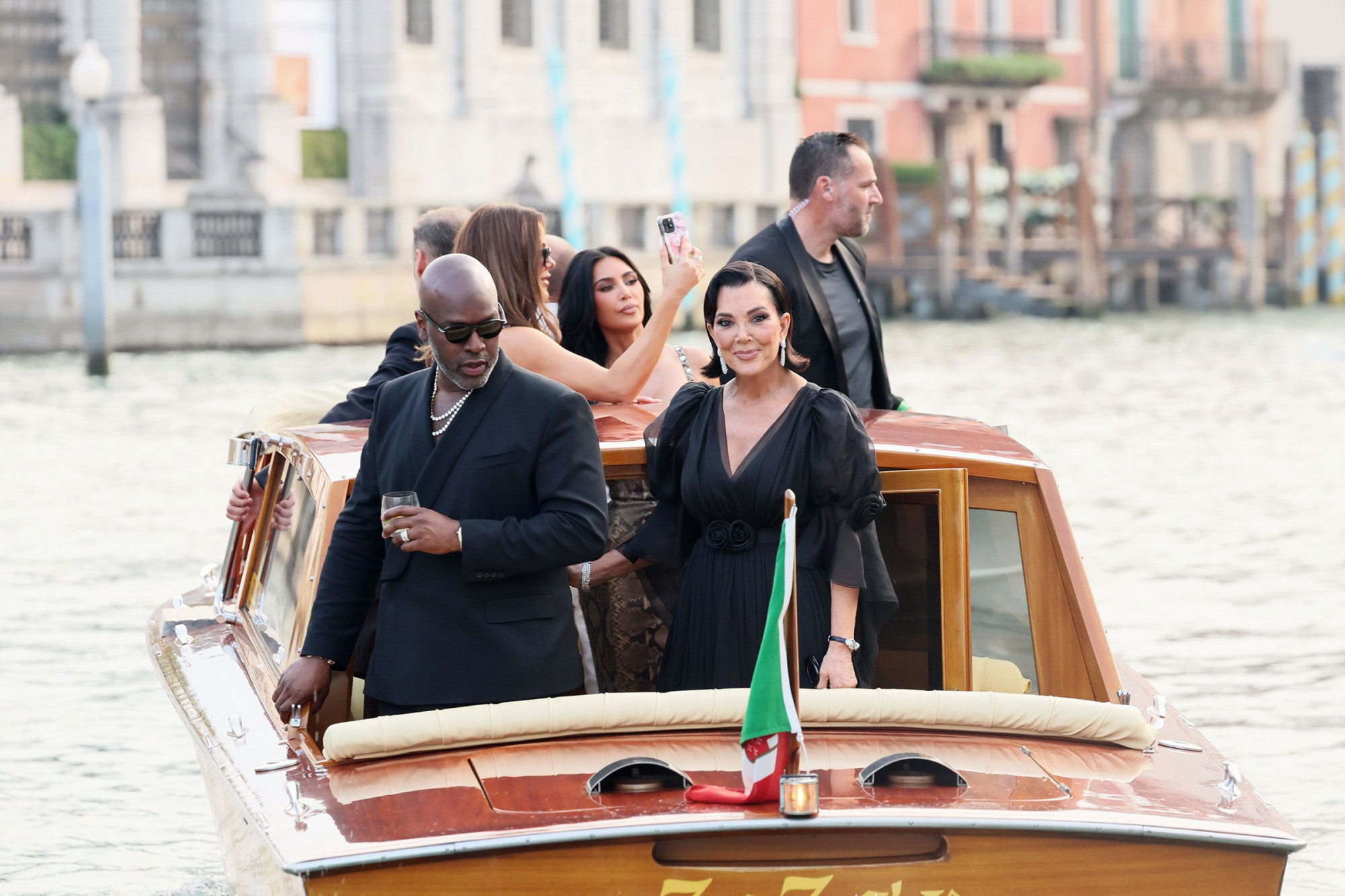 Khi lễ cưới hoá sàn diễn thời trang Trong bức ảnh ghi lại khoảnh khắc trên du thuyền tại Venice trong khuôn khổ lễ cưới tỷ phú Jeff Bezos, Kris Jenner – “mẹ Kim Kardashian” – xuất hiện với vẻ ngoài đầy quyền lực và sang trọng. Bà diện một chiếc váy đen dài chất liệu voan nhẹ, có tay phồng và chiết eo duyên dáng với điểm nhấn là chi tiết hoa cài tại eo. Thiết kế cổ chữ V sâu giúp tôn lên phần cổ và vai, mang lại vẻ thanh lịch cổ điển.