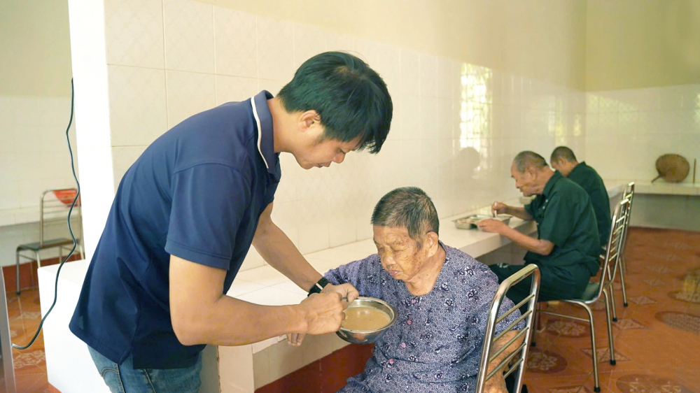 Y tá Quách Văn Thịnh chăm sóc bữa ăn cho một nữ thương bệnh binh tâm thần  không còn khả năng tự phục vụ - ẢNH: NGUYỄN QUANG