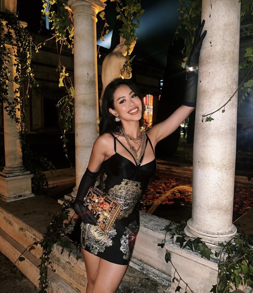 Chiếc đầm mini ôm sát, chất liệu satin kết hợp họa tiết baroque cầu kỳ mang đậm dấu ấn của Dolce & Gabbana giúp Tiên Nguyễn ghi điểm phong cách gợi cảm, quyền lực. Điểm nhấn của outfit nằm ở loạt phụ kiện gồm clutch đính đá lấp lánh, găng tay voan đen và chuỗi dây chuyền layering bản to, tạo nên vẻ ngoài sang chảnh 