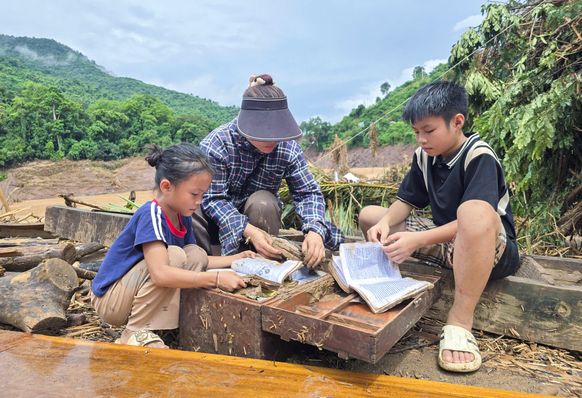 Chị Tha cùng 2 con bên rương sách cũ ngập ngụa trong bùn đất - Ảnh: Phan Ngọc
