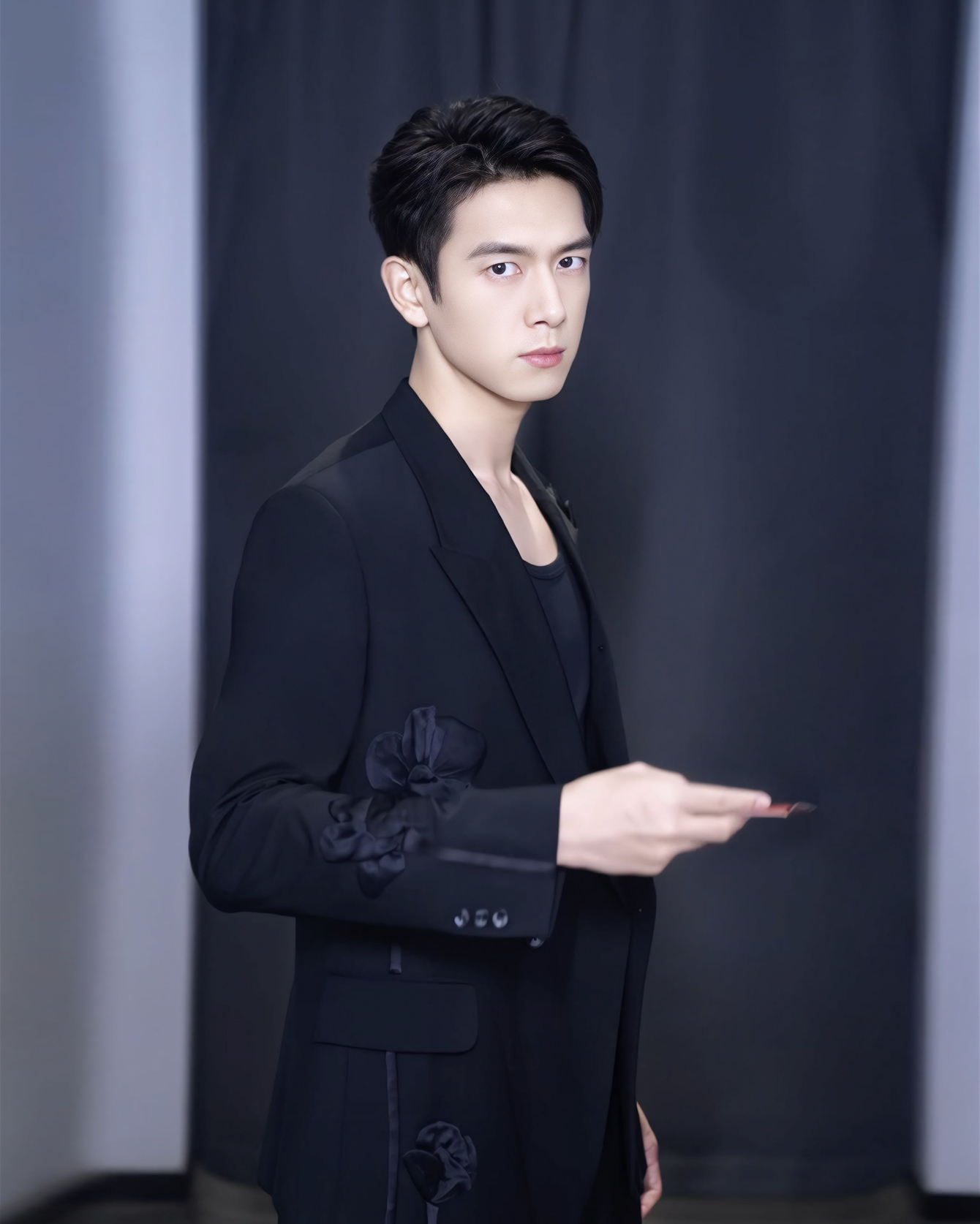 Diện bộ vest đen đính hoa, Lý Hiện toát lên vẻ lịch lãm và cuốn hút với phong cách thời trang sang trọng, hiện đại. Kiểu tóc được chải gọn gàng, gương mặt lạnh lùng với ánh mắt sắc sảo càng làm nổi bật khí chất nam tính, điềm đạm. Theo chia sẻ từ nhà thiết kế Trần Hùng, trang phục này là một trong những mẫu chủ đạo trong bộ sưu tập Xuân Hè 2025 từng ra mắt tại London Fashion Week. 