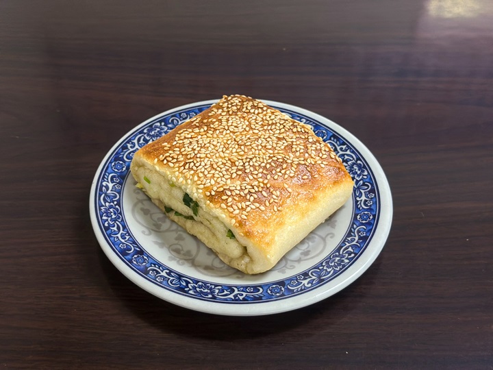 Bánh mì dẹt hành lá có vỏ vàng giòn, ngọt thanh và thơm mùi mè. Bột bánh dai, thơm được nhồi hành lá và một chút tiêu. Bánh đơn giản nhưng vô cùng hấp dẫn. Địa chỉ: Quán sữa đậu nành Yonghe Chia Hsiang, số 57 đường Mẫn Trí, quận Vĩnh Hòa - Ảnh: MICHELIN