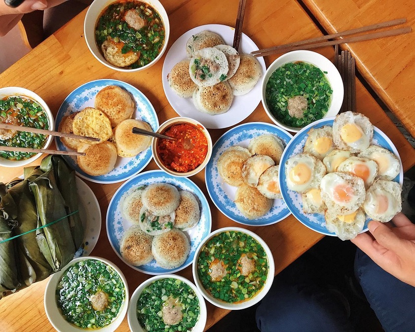 Bánh căn Nha Trang là món ăn dân dã nhưng lại khiến du khách mê mẩn ngay từ lần thử đầu tiên. Những chiếc bánh nhỏ, tròn, được đổ trong khuôn đất nung, nóng hổi và giòn rụm. Nhân bánh đa dạng, từ trứng cút, tôm, mực đến thịt bò, vừa dân dã vừa đậm đà hương vị biển. Điểm đặc biệt làm nên sự khác biệt chính là nước chấm: pha từ nước mắm, mỡ hành, xoài bằm và đôi khi thêm xíu xíu mắm nêm. Khi ăn, thực khách thường kèm rau sống, tạo nên sự hài hòa giữa vị béo, ngọt, chua cay