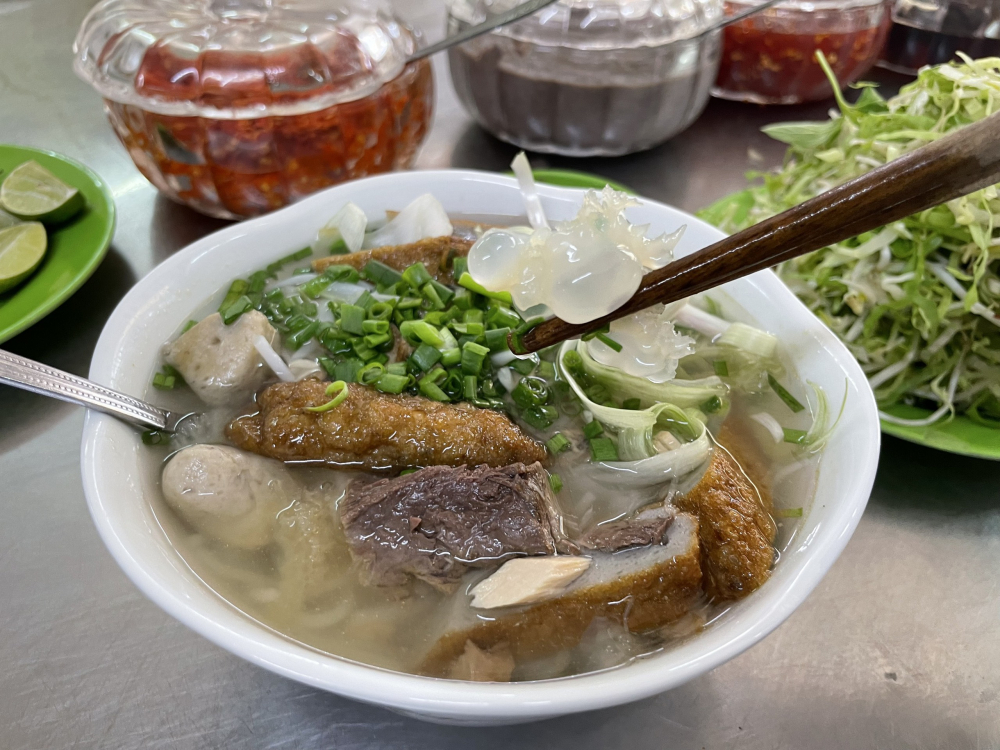 Bún sứa là một món đặc sản của vùng biển Nha Trang. Món ăn này có thành phần chính là bún tươi, sứa tươi (đã được sơ chế kỹ càng) và nước lèo được nấu từ cá, tôm, hoặc xương heo. Ngoài ra, còn có các món ăn kèm khác như chả cá, cá dầm, rau sống, ớt, chanh, mắm tôm... để tăng thêm hương vị. Khi ăn bạn sẽ cảm nhận được sứa tươi, giòn sần sật, kết hợp với vị ngọt thanh của nước lèo và hương vị đặc trưng của các loại gia vị đi kèm, tạo nên một món ăn hấp dẫn và độc đáo. Một địa chỉ mà bạn có thể đến để thử món ăn này nằm ở 24 Hàn Thuyên - Ảnh: MIA
