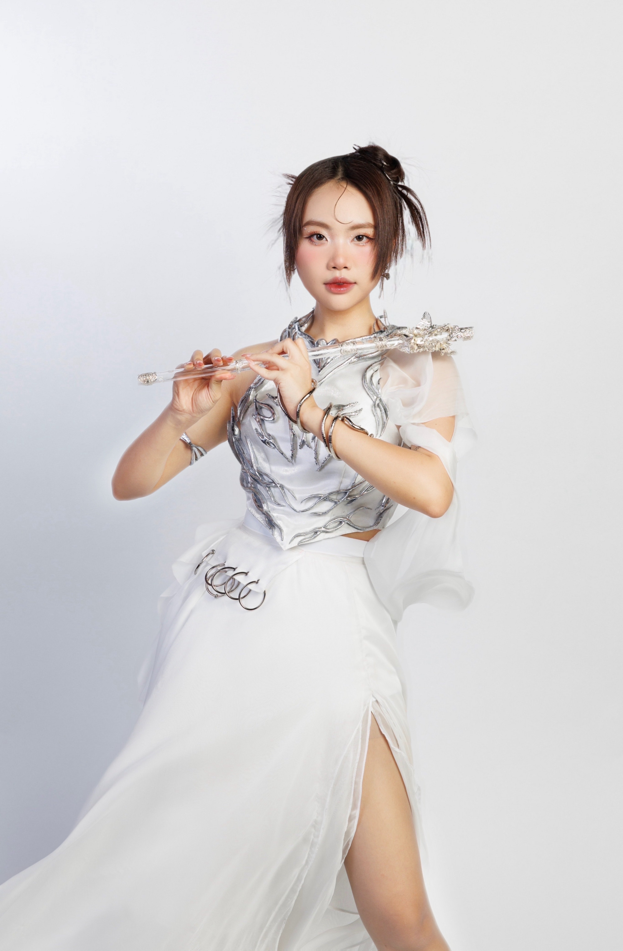 phong cách trang điểm vừa ngọt ngào vừa sắc sảo. Làn da được xử lý mịn màng, tươi sáng. Đôi mắt nhấn bằng eyeliner mảnh, kết hợp mi dài cong vút và phấn mắt ánh hồng nhẹ, tạo cảm giác long lanh. Má hồng tán cao mang lại vẻ trẻ trung, trong khi đôi môi son đỏ hồng căng mọng làm điểm nhấn nổi bật. Tổng thể makeup giúp gương mặt cô vừa thanh thoát, nữ tính vừa toát lên khí chất hiện đại, rất hài hòa với trang phục trắng ánh bạc.