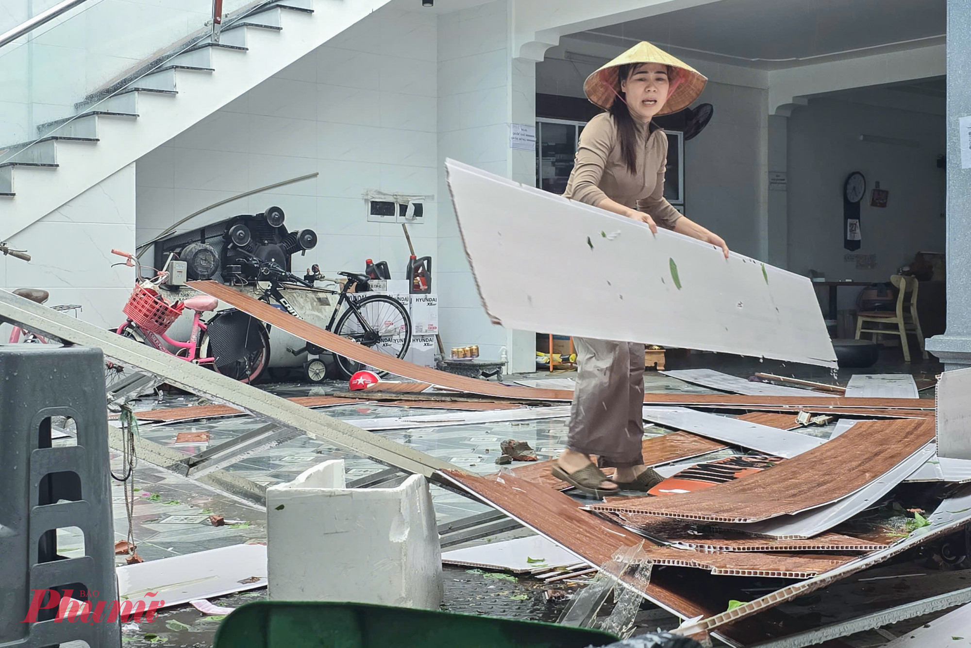 Chị Lộc nhặt lại những tấm trần nhựa còn nguyên vẹn để lợp lại mái nhà sau bão 