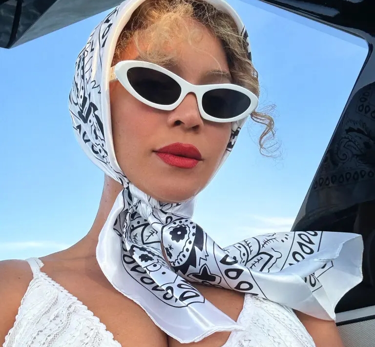 Beyoncé mang đến một hình ảnh sang trọng và gợi cảm khi diện khăn đội đầu lụa họa tiết đen trắng, buộc gọn dưới cằm theo phong cách cổ điển. Cô khéo léo kết hợp cùng mắt kính mắt mèo trắng viền dày, tạo nên vẻ ngoài vừa retro vừa hiện đại.