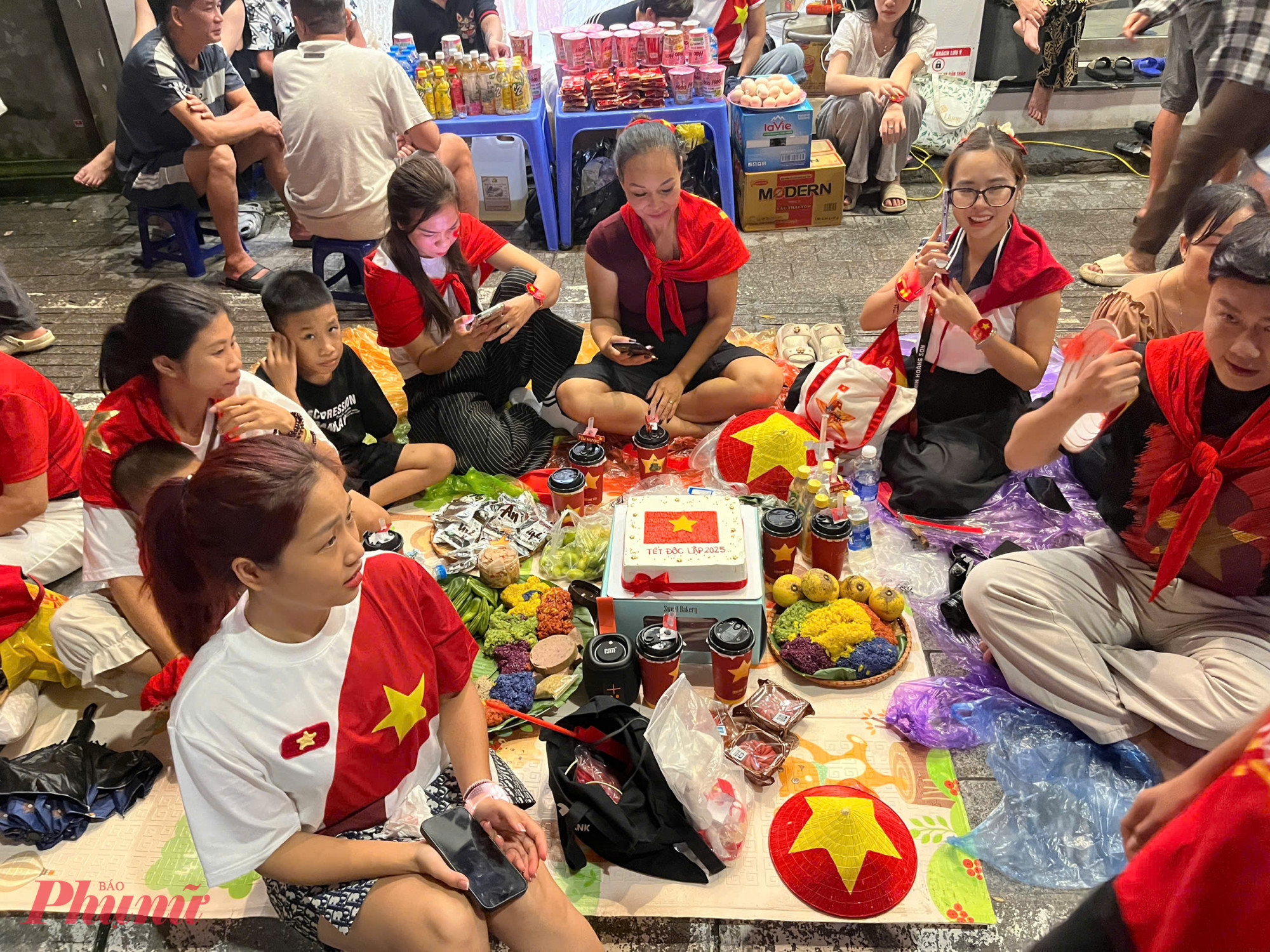 Không khí đêm trước tổng duyệt trở nên đặc biệt khi nhiều gia đình bày biện mâm cỗ nhỏ, trang trí rực rỡ để mừng ngày đại lễ, vừa tạo điểm nhấn, vừa mời mọi người cùng thức đêm. Một cửa hàng lẩu còn chuẩn bị tới 200 bát bún, mì phát miễn phí cho người dân, ưu tiên trẻ em.