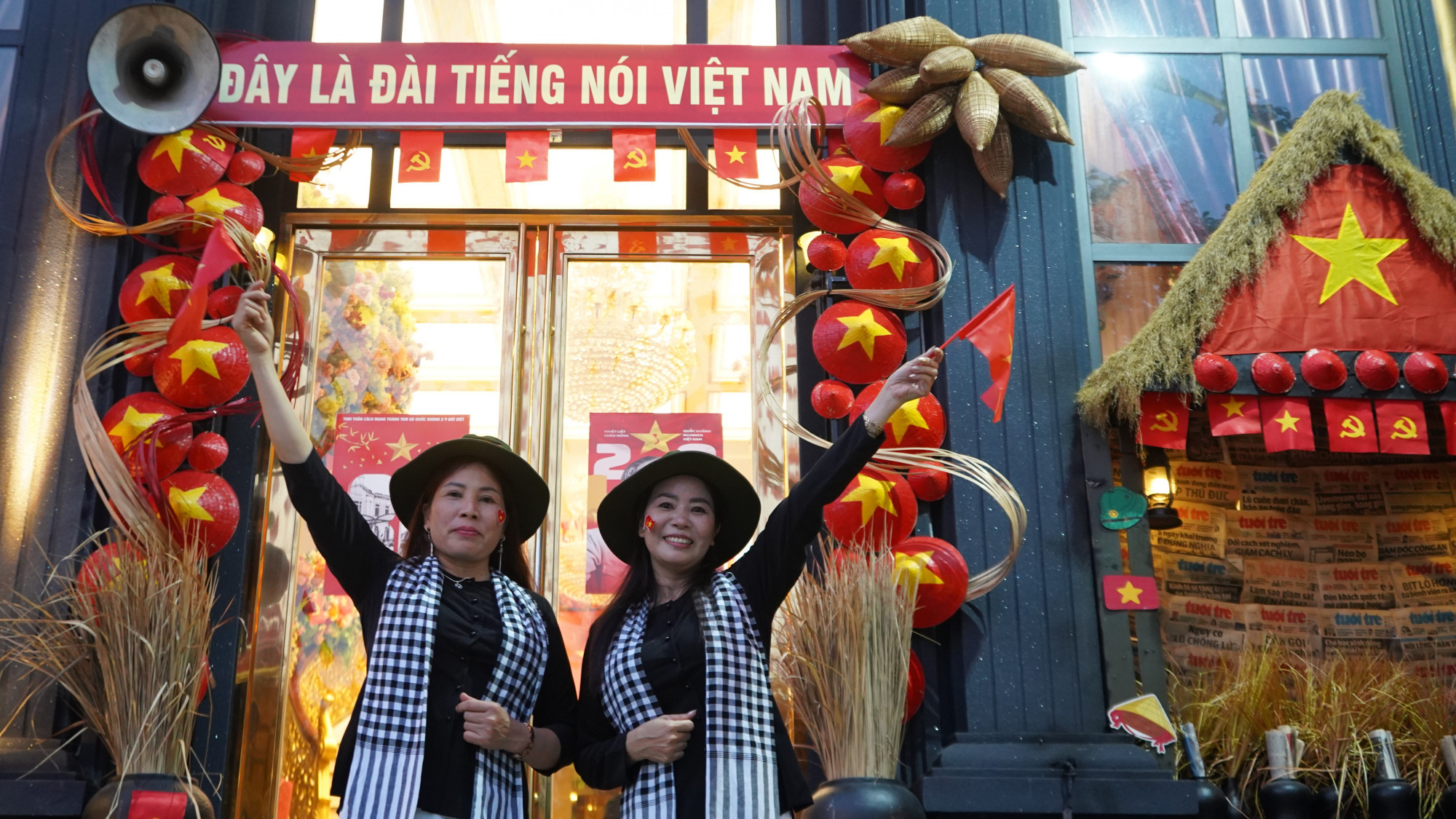 Không chỉ giới trẻ, các cô cũng đu trend áo bà ba, khăn rằn, giơ cao cờ Tổ quốc trước cổng chào “Đây là Đài Tiếng nói Việt Nam” – biểu tượng thời chiến - Ảnh: Nhật Khôi