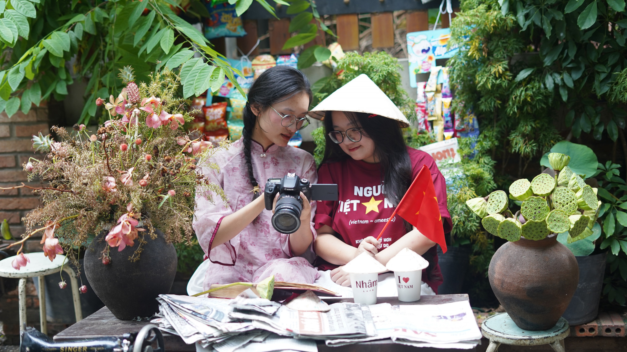Hai bạn trẻ cùng nhau xem lại hình ảnh vừa chụp trong không gian mang đậm chất xưa với bàn gỗ, máy khâu, hoa sen - Ảnh: Như Ý