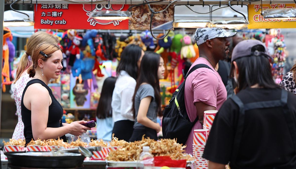Du khách quốc tế dạo quanh các quầy hàng thực phẩm tại khu mua sắm và du lịch trung tâm Myeong-dong của Seoul - Ảnh: Yonhap
