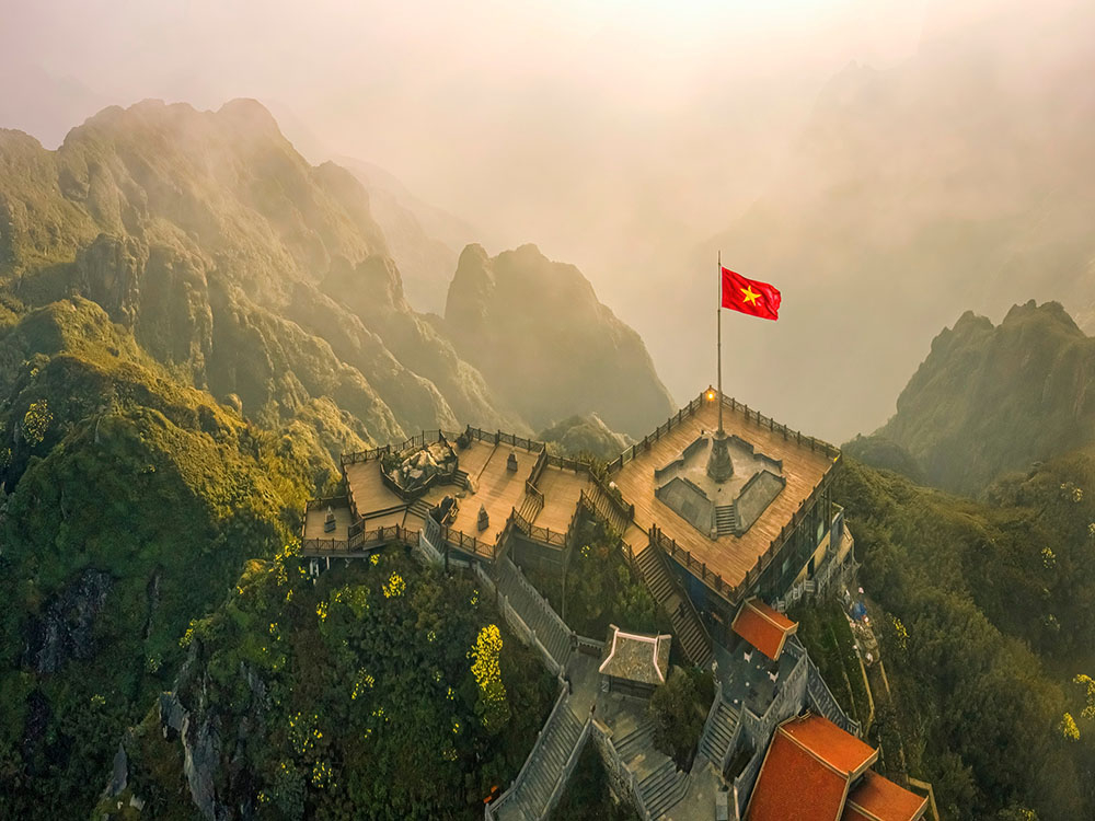 Chinh phục đỉnh Fansipan – ngọn núi cao nhất Việt Nam với độ cao 3.147,3 mét – từ lâu đã trở thành “huy hiệu” danh dự của dân phượt ba lô. Đứng trên đỉnh, phóng tầm mắt ra biển mây bồng bềnh cùng những dãy núi đá gồ ghề kéo dài bất tận, du khách không khỏi choáng ngợp trước vẻ đẹp hùng vĩ. Hành trình chinh phục có thể gói gọn trong một ngày, với những bước chân lấm bùn xuyên qua rừng rậm, leo dốc trơn trượt và lối mòn rễ cây chằng chịt; hoặc thong thả hơn khi dừng lại cắm trại trên sườn núi để tận hưởng thiên nhiên. Dù chọn cách nào, đó cũng là một thử thách đòi hỏi sức bền. Ngày nay, du khách còn có thể dễ dàng “chạm mây” chỉ trong 15 phút nhờ tuyến cáp treo hiện đại – lựa chọn hoàn hảo cho những ai muốn chiêm ngưỡng cảnh sắc ngoạn mục mà không cần đổ nhiều mồ hôi - Ảnh: Wanderlust