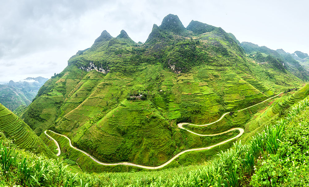 Hà Giang, nơi địa đầu cực Bắc của Việt Nam, sở hữu vẻ đẹp núi non và ruộng bậc thang không hề kém cạnh Sa Pa, nhưng lại vắng bóng du khách trekking hơn nhiều. Phần lớn khách đến đây chọn chinh phục cung đường đèo Hà Giang Loop bằng xe máy hoặc ô tô trong 2–3 ngày, men theo những dãy núi hùng vĩ. Thế nhưng, đi bộ mới thật sự giúp bạn “chạm” vào cảnh sắc nơi này. Trekking Mã Pí Lèng mang đến tầm nhìn ngoạn mục: khi làn sương tan dần, hiện ra ngôi làng nhỏ dưới thung lũng sâu; tia nắng lọt qua mây rọi xuống người nông dân đội nón lá đang cày cấy trên những thửa ruộng bậc thang. Đỉnh đèo, chạm tới bằng con đường mòn trên trời chỉ mất khoảng hai giờ đi bộ, mở ra khung cảnh hùng tráng: núi rừng trập trùng, những ngọn núi rừng phủ xanh sừng sững, dưới chân là dòng Nho Quế uốn lượn như dải lụa. Bạn có thể chọn cung đường này như một trải nghiệm nhỏ trong hành trình Hà Giang Loop, hoặc kết hợp thành chuyến trekking nhiều ngày để thật sự rời xa dòng khách ba lô, hòa mình vào đời sống văn hóa của người H’Mông, người Tày nơi miền biên viễn - Ảnh: Wanderlust