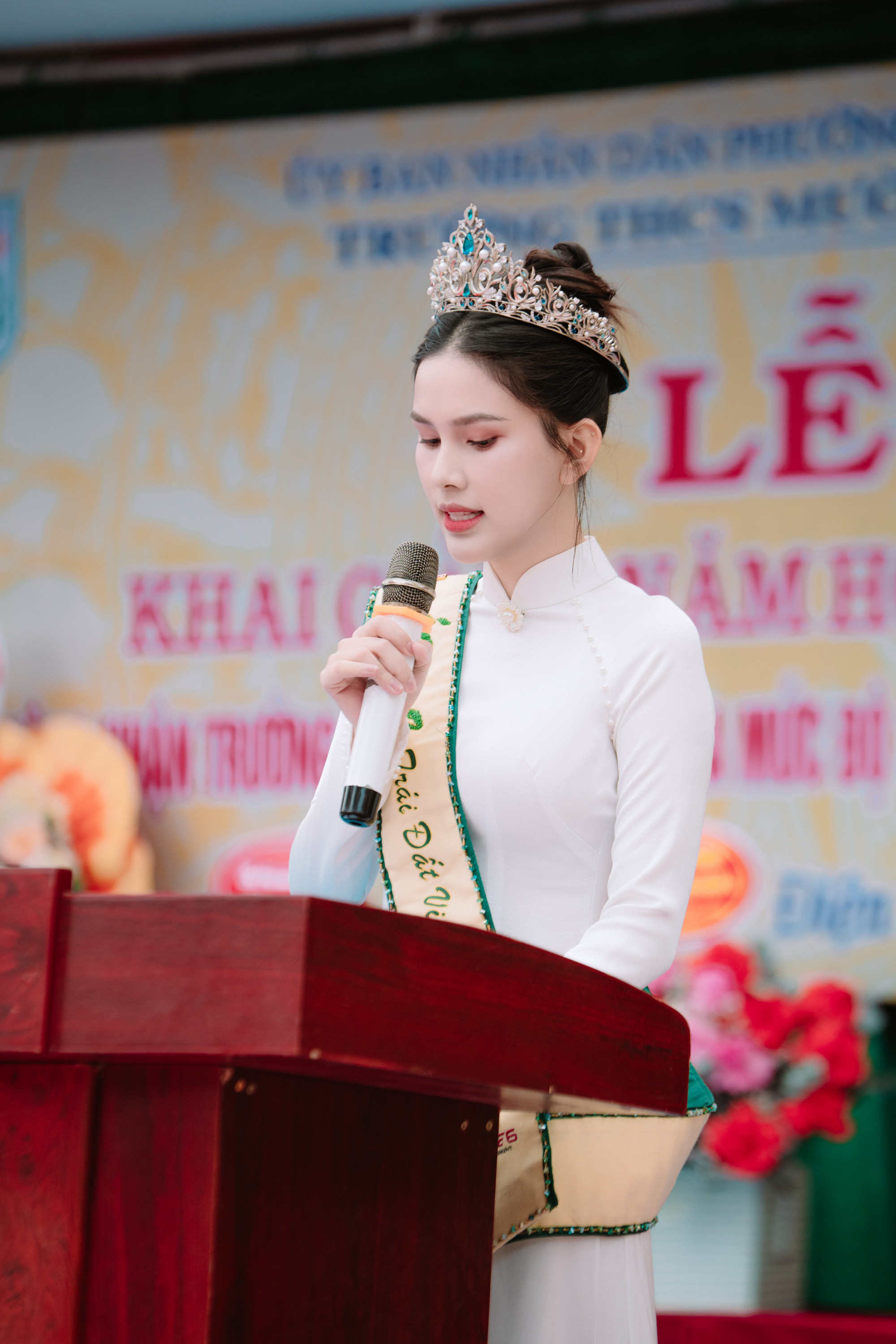 Gương mặt Linh Đan được trang điểm nhẹ nhàng với lớp nền mịn màng, đôi môi hồng tươi tắn và hàng mi cong tự nhiên, giữ trọn sự trong sáng mà vẫn nổi bật giữa đám đông. Mái tóc búi cao gọn gàng làm nổi bật những đường nét thanh tú và khí chất trang nhã.