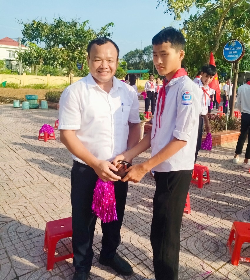 Ông Nguyễn Xuân Khánh, Phó Bí thư Thường trực Đảng ủy xã Bích Hào tháo dây thắt lưng tặng học sinh lớp 8 sau lễ khai giảng năm học mới. Ảnh: Trần Đình Thơ.