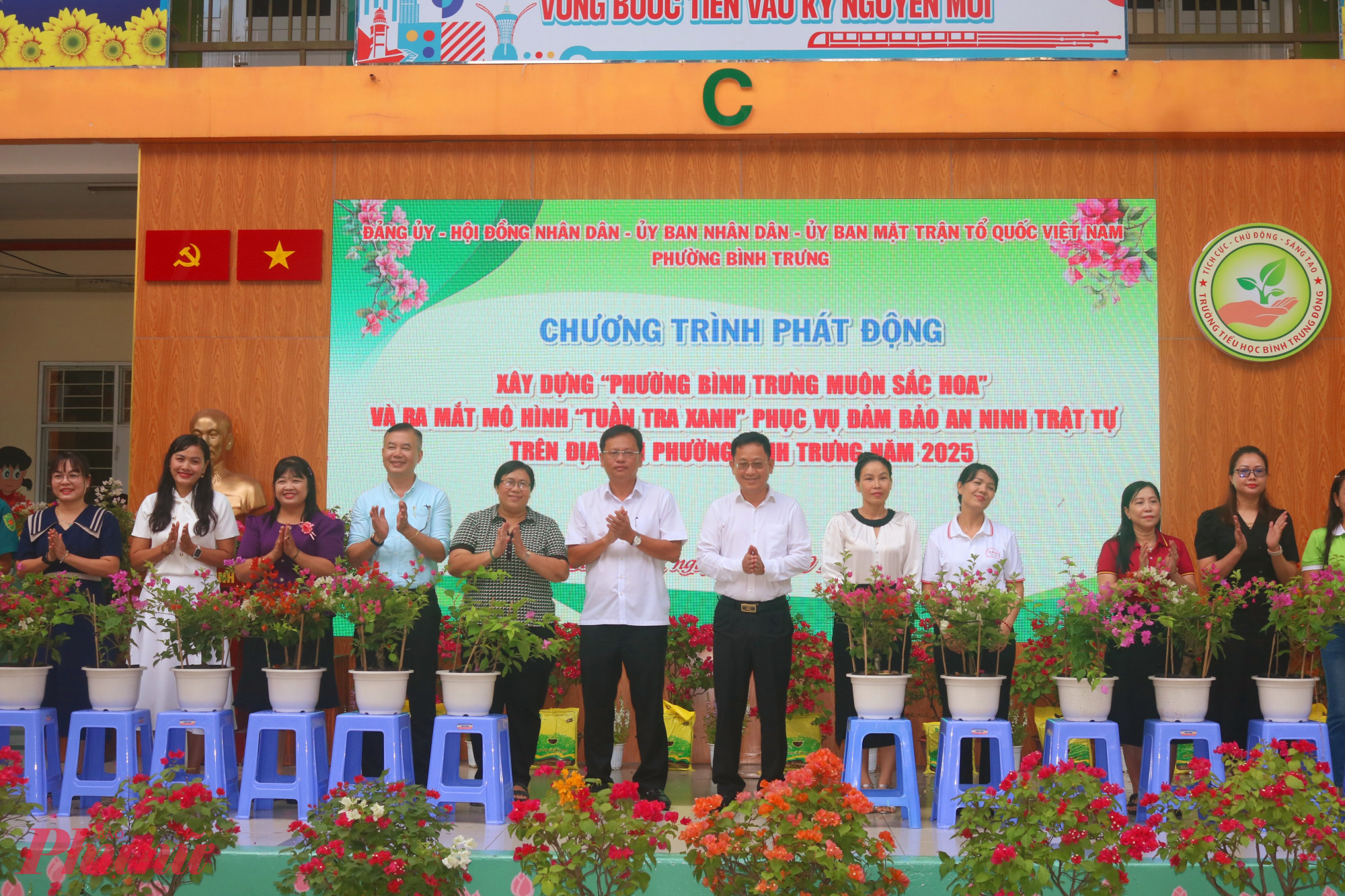 Ông Trần Quốc Trung – Bí thư Đảng ủy, Chủ tịch HĐND phường Bình Trưng (thứ 7, từ trái qua) và ông Lê Quang Nam – Phó bí thư thường trực Đảng ủy phường Bình Trưng (thứ 6, từ trái qua) – trao chậu hoa giấy đến đại diện các khu phố - Ảnh: Mẫn Nhi