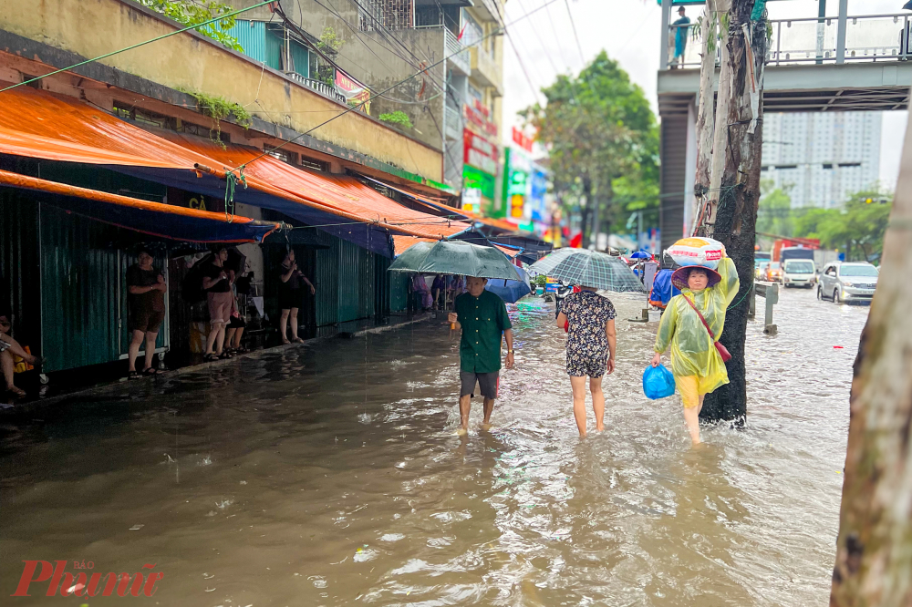 Nước ngập lên cả vỉa hè đoạn đối diện bệnh viện K, nhiều người đưa bệnh nhân đi thăm khám phải đợi ở ngoài trên vỉa hè do chưa tới giờ vào thăm bệnh nhân.