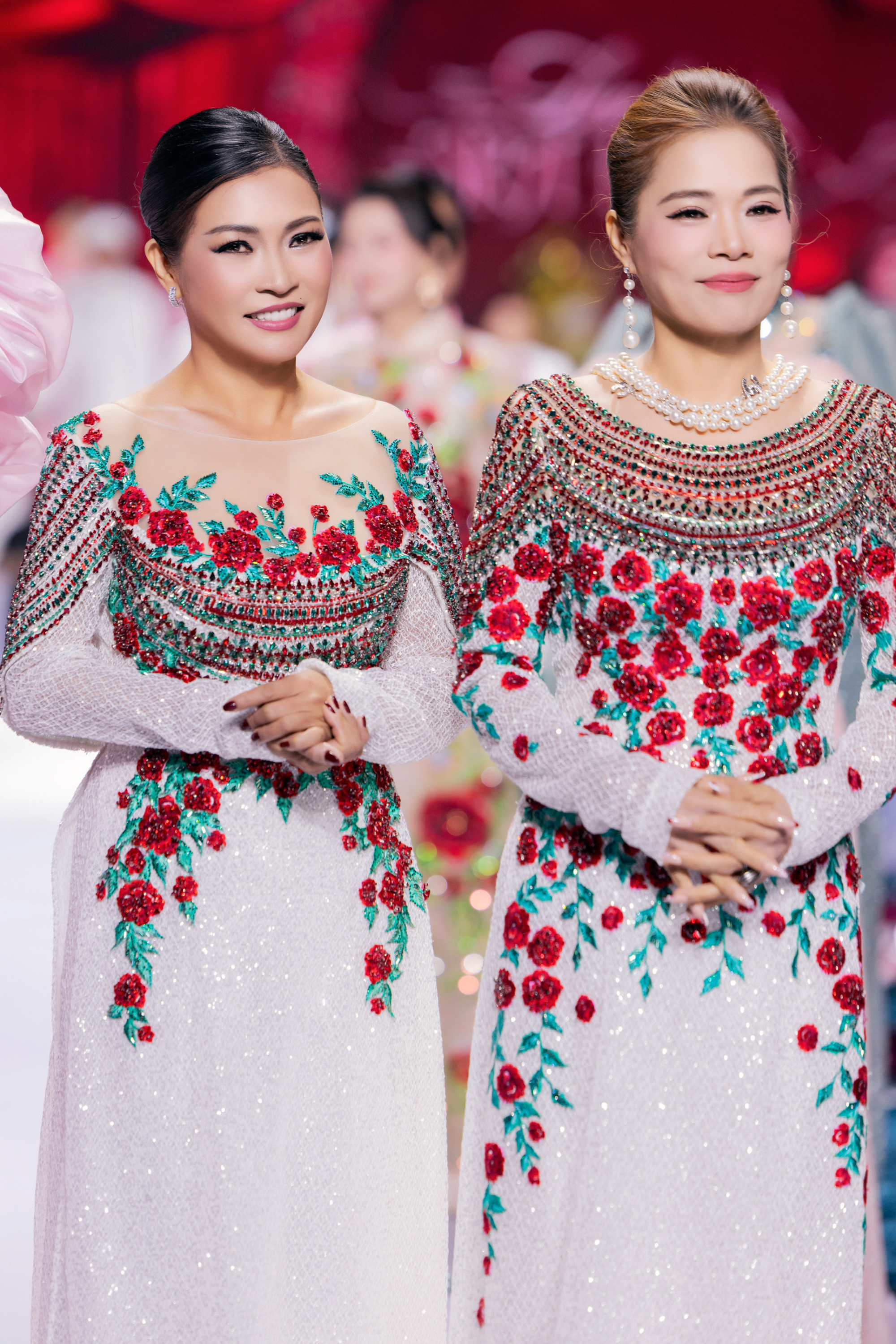 Phương Thanh và Mỹ Lệ xuất hiện nổi bật trên sàn diễn trong hai bộ áo dài đồng điệu, mang sắc trắng chủ đạo điểm xuyết hoa hồng đỏ thêu nổi, kết hợp cùng chi tiết đính kết lấp lánh tạo hiệu ứng sang trọng.  Cả hai nghệ sĩ chọn kiểu tóc búi cao gọn gàng, trang điểm nền nã, tôn lên gương mặt rạng rỡ và thần thái tự tin. T