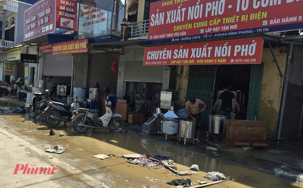 Lớp bùn dày đặc phủ kín mặt đường và tường nhà, người dân lội trong bùn, khẩn trương dọn dẹp từng món đồ ướt sũng.