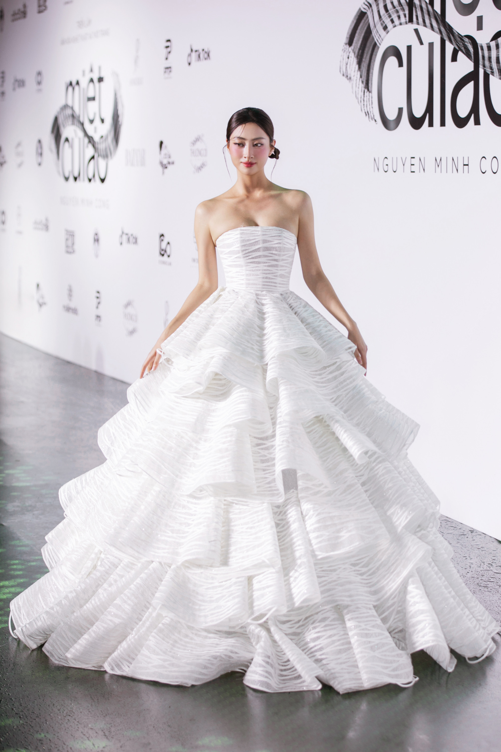 Hoa hậu Lương Thùy Linh trong thiết kế “Bánh tráng rế”. NTK sử dụng lớp ren trắng được đan xen từng tầng, tạo hiệu ứng cong mềm đặc trưng của bánh rế. Tổng thể trang phục mang vẻ đẹp nhẹ nhàng, thướt tha, gợi hình ảnh người con gái miền Tây duyên dáng giữa dòng nước lững lờ.