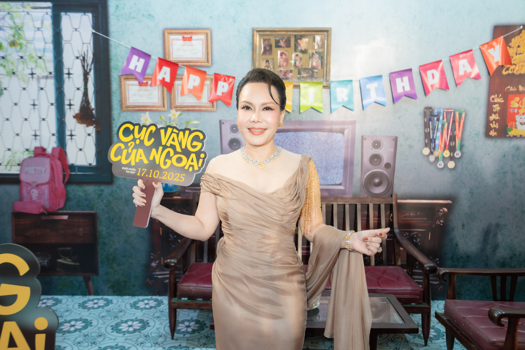 Diễn viên Việt Hương ghi điểm với vẻ ngoài sang trọng và đằm thắm trong bộ đầm dạ hội màu champagne ánh đồng. Thiết kế ôm dáng tinh tế, vai trễ và phần tay áo buông nhẹ điểm chuỗi tua rua vàng giúp tôn lên nét quý phái, nữ tính. Phụ kiện vòng cổ và vòng tay kim cương góp phần hoàn thiện vẻ đẹp thanh lịch, kiểu tóc búi cao gọn gàng và lớp trang điểm tông cam đất mang lại vẻ trẻ trung.