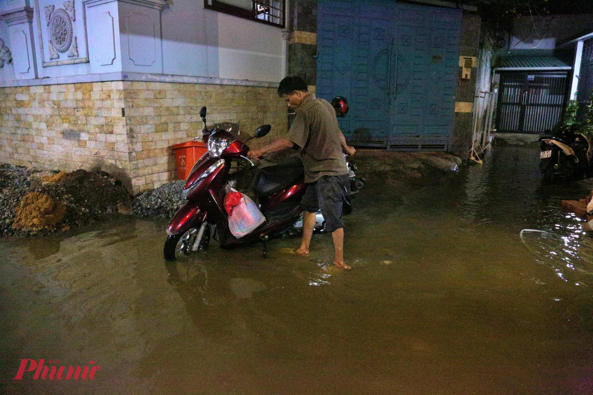 Người đàn ông phải dắt xe máy lên chỗ cao để tránh bị ngập.
