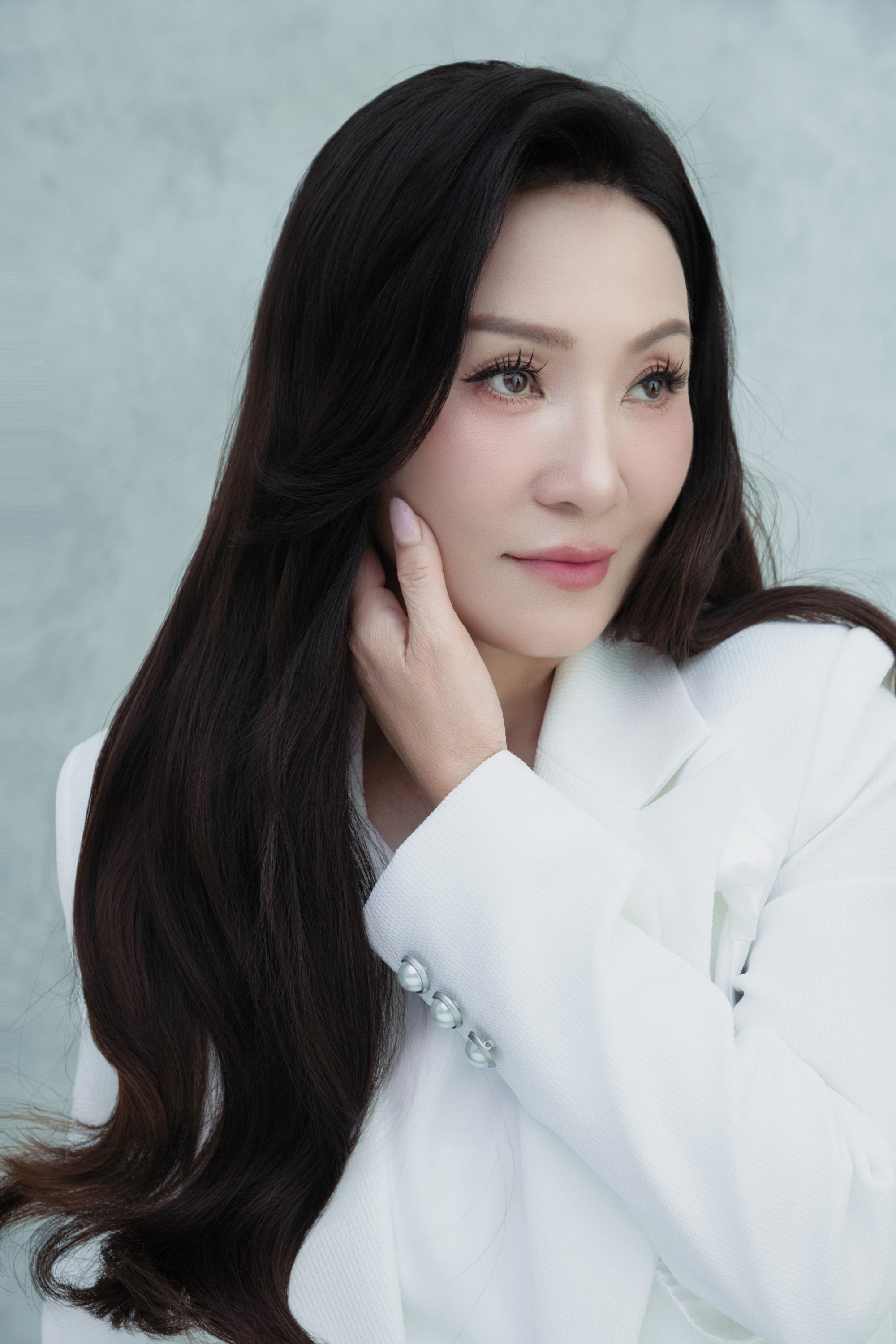 Làn da mịn màng, sáng khỏe giúp gương mặt cô trông rạng rỡ dù chỉ trang điểm nhẹ nhàng với tông hồng pastel tinh tế. Đôi mắt trong trẻo, hàng mi cong tự nhiên mang đến ánh nhìn dịu dàng nhưng đầy sức sống. Mái tóc dài đen óng được chăm chút kỹ, buông mềm qua vai tạo nên nét mềm mại, nữ tính.