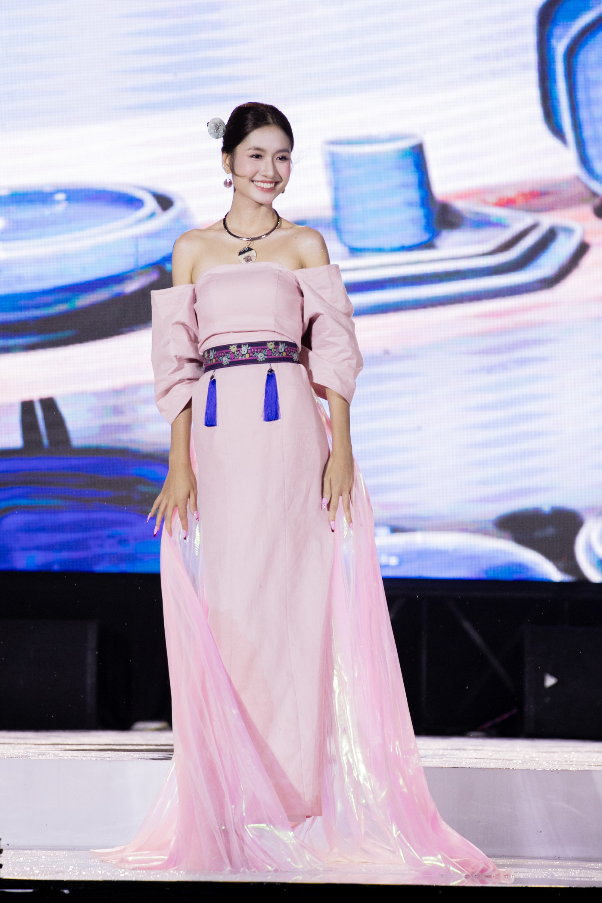 Cô chọn phong cách trang điểm tự nhiên với lớp nền trong suốt, má hồng nhẹ và đôi môi hồng phớt đồng điệu với trang phục. Mái tóc được búi gọn giúp tôn lên gương mặt rạng rỡ, duyên dáng. Người đẹp mong muốn lan tỏa thông điệp tích cực đến với mọi người ''xanh, sạch và bảo vệ môi trường''.