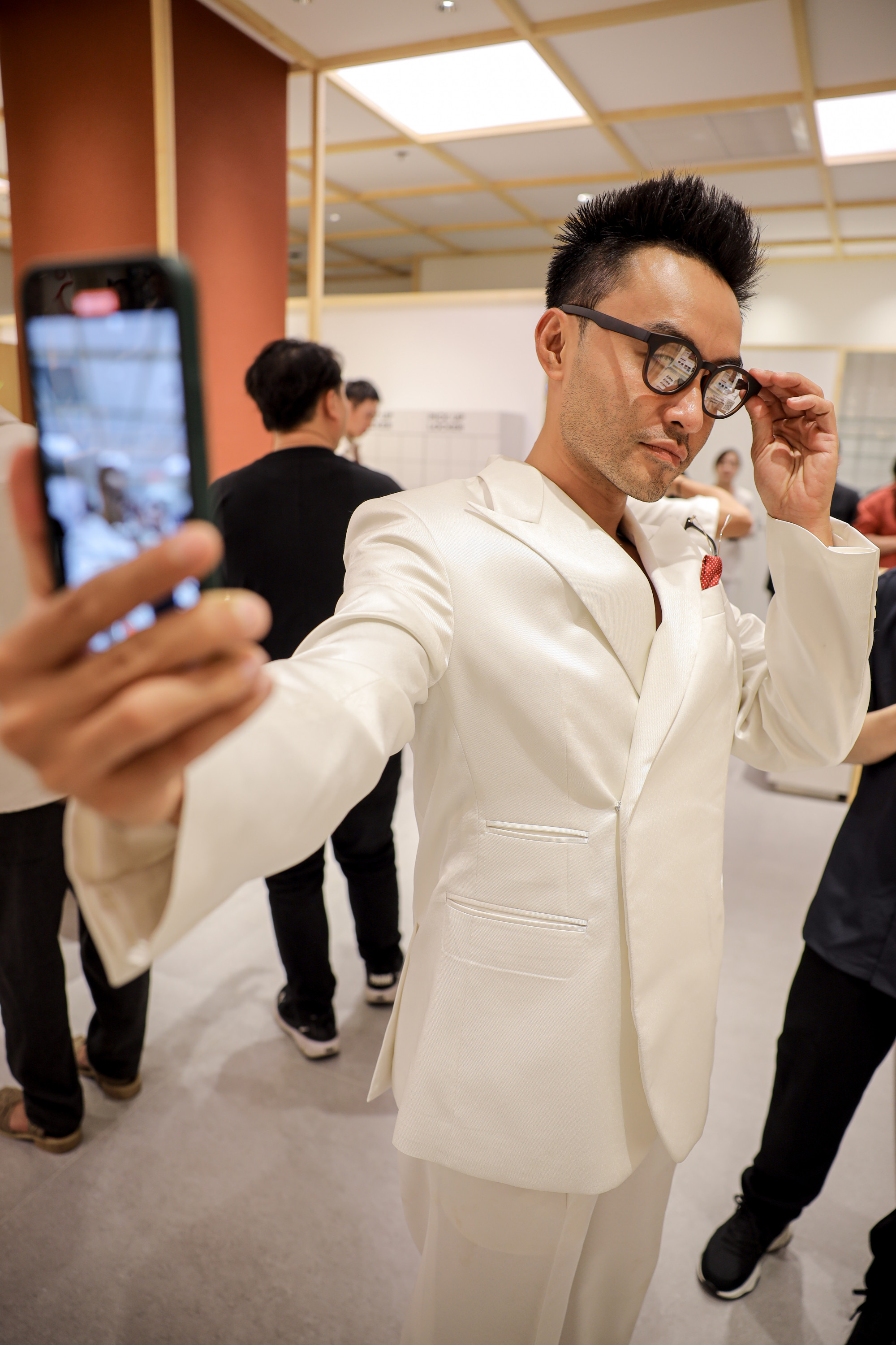 MC Dustin Phúc Nguyễn diện bộ suit trắng kem được cắt may chuẩn phom, tạo vẻ ngoài vừa lịch lãm vừa hiện đại. Anh phối kèm chiếc kính gọng đen bản nhỏ giúp tôn lên vẻ thông minh, sành điệu, cân bằng hoàn hảo giữa sự cổ điển và hiện đại.