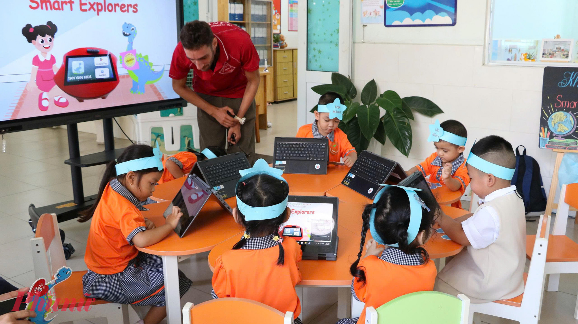 Khu vực Smart Explorers (Nhà thám hiểm nhí thông minh)  tại phòng học thông minh với TV tương tác, máy tính bảng, bộ câu hỏi, bàn, ghế. Giáo viên hiển thị câu hỏi trên màn hình TV. 