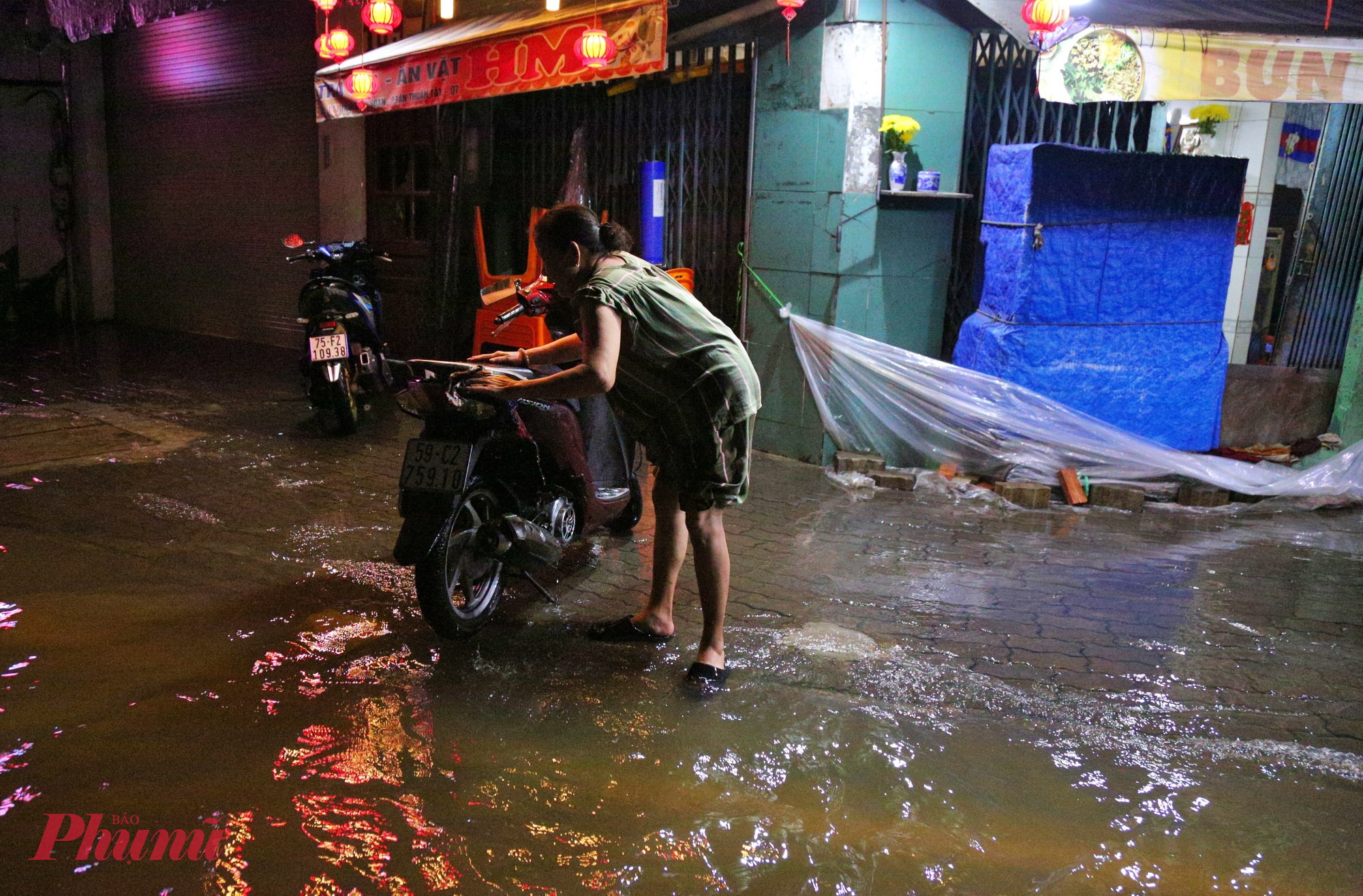 Người phụ nữ tranh thủ dắt xe máy ra rửa trong lúc triều cường đạt đỉnh. 