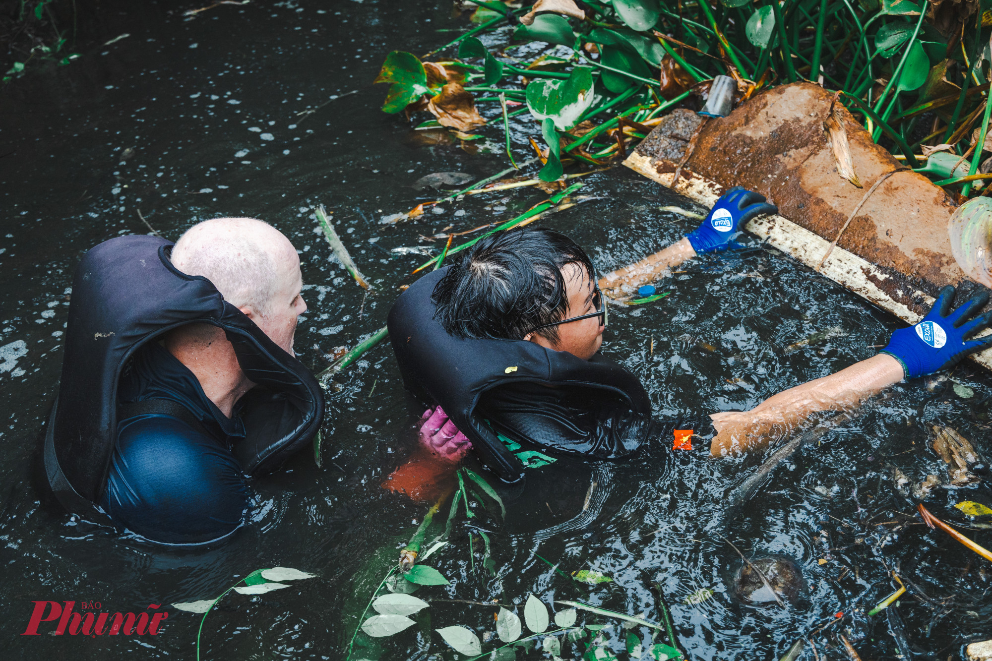 Theo phân công trước đó, một nhóm sẽ đứng trên bờ kênh phân luồn giao thông và giữ dây cho một nhóm được trang bị áo phao, đồ bảo hộ lội dưới kênh để vớt rác, lục bình lên.