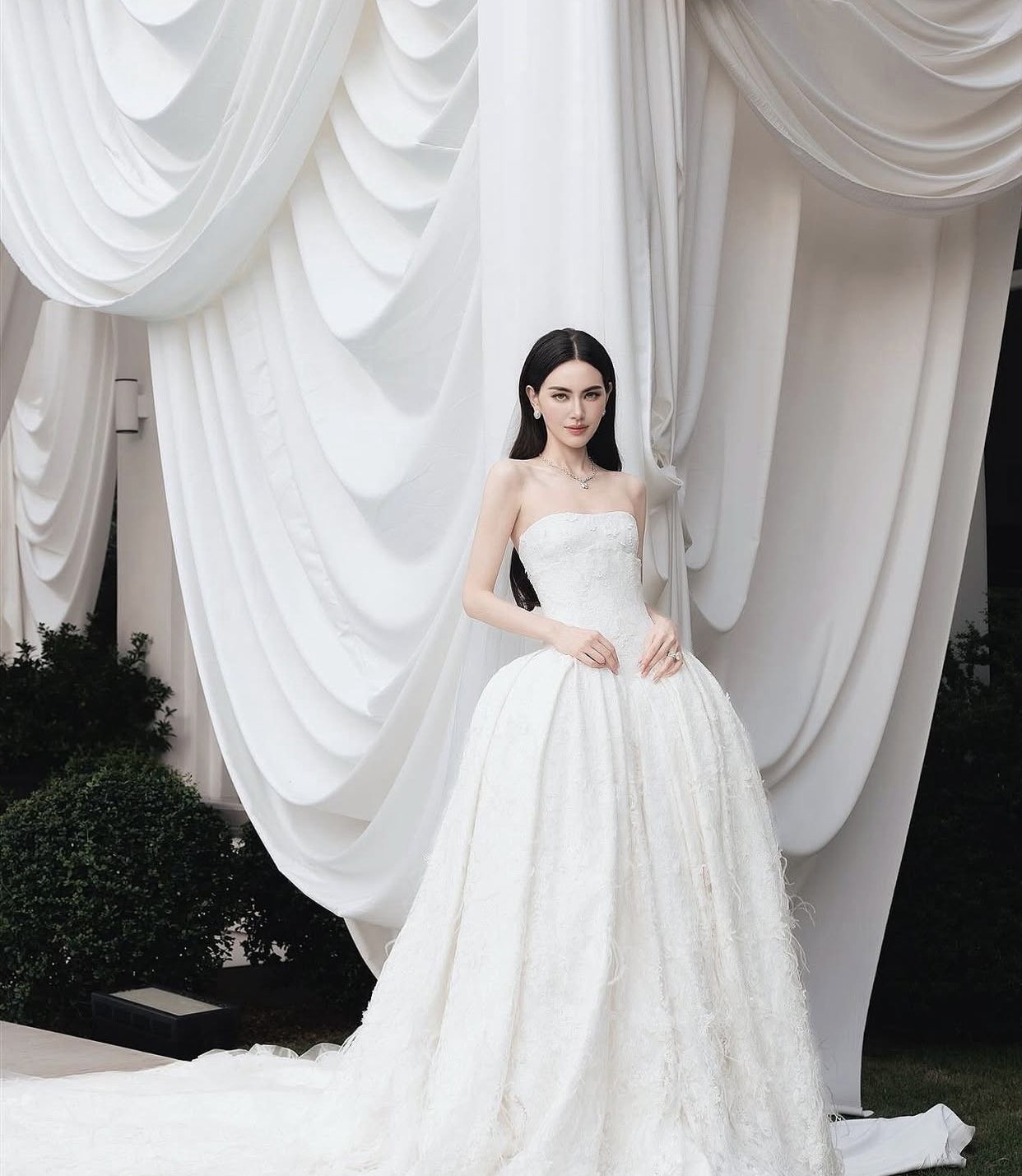 Nổi bật giữa khung cảnh được trang trí tinh tế với hoa trắng và gam màu trung tính, Mai Davika xuất hiện tựa nàng thơ bước ra từ cổ tích trong thiết kế váy cưới độc quyền của Gucci. Chiếc váy trễ vai dáng cúp ngực ôm sát phần thân trên, tôn lên vóc dáng mảnh mai và bờ vai thanh thoát của nữ diễn viên.