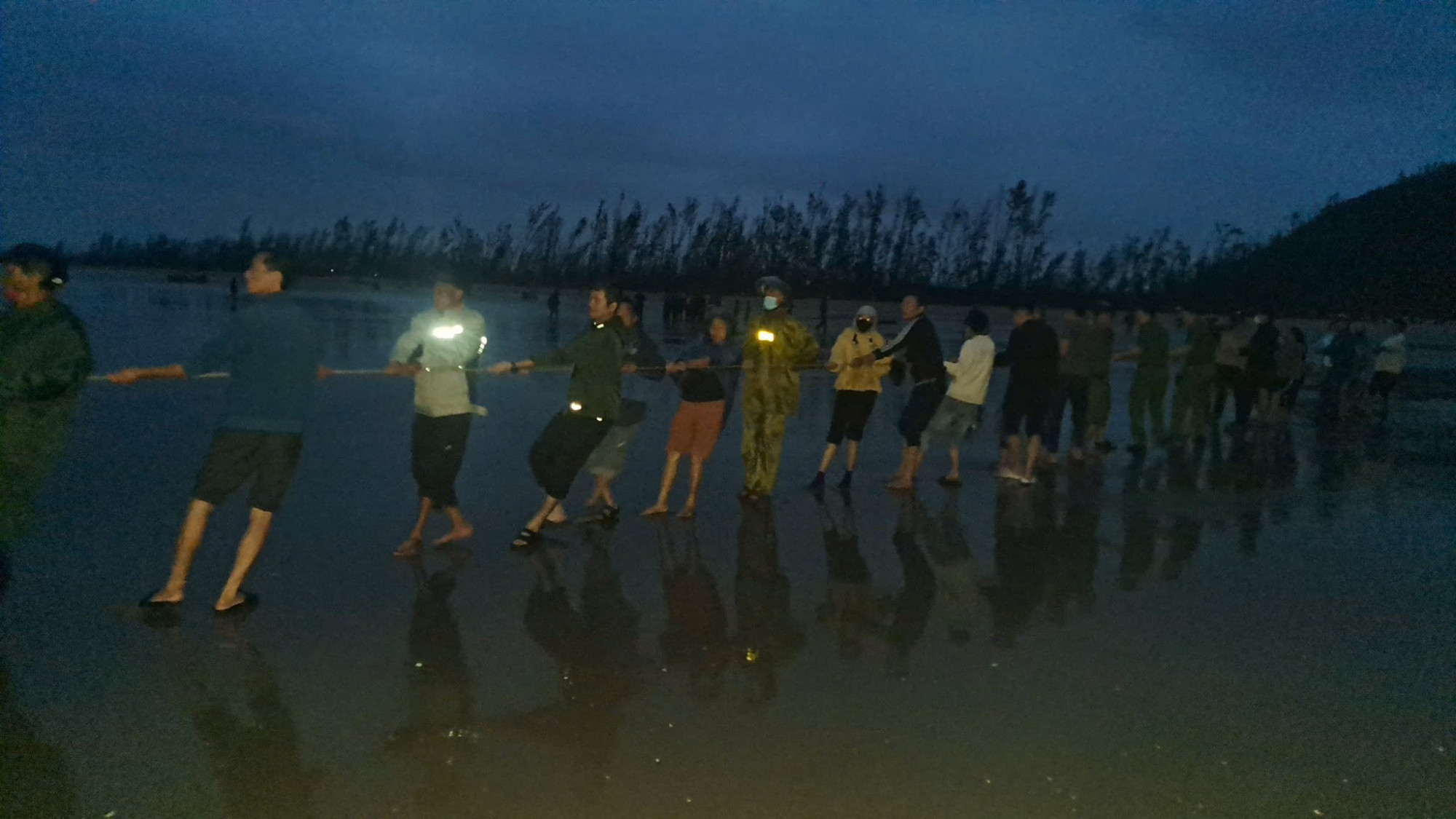 Các lực lượng chức năng cùng người dân hợp sức kéo thuyền đánh cá bị chìm vào bờ - Ảnh: Hoàng Trang