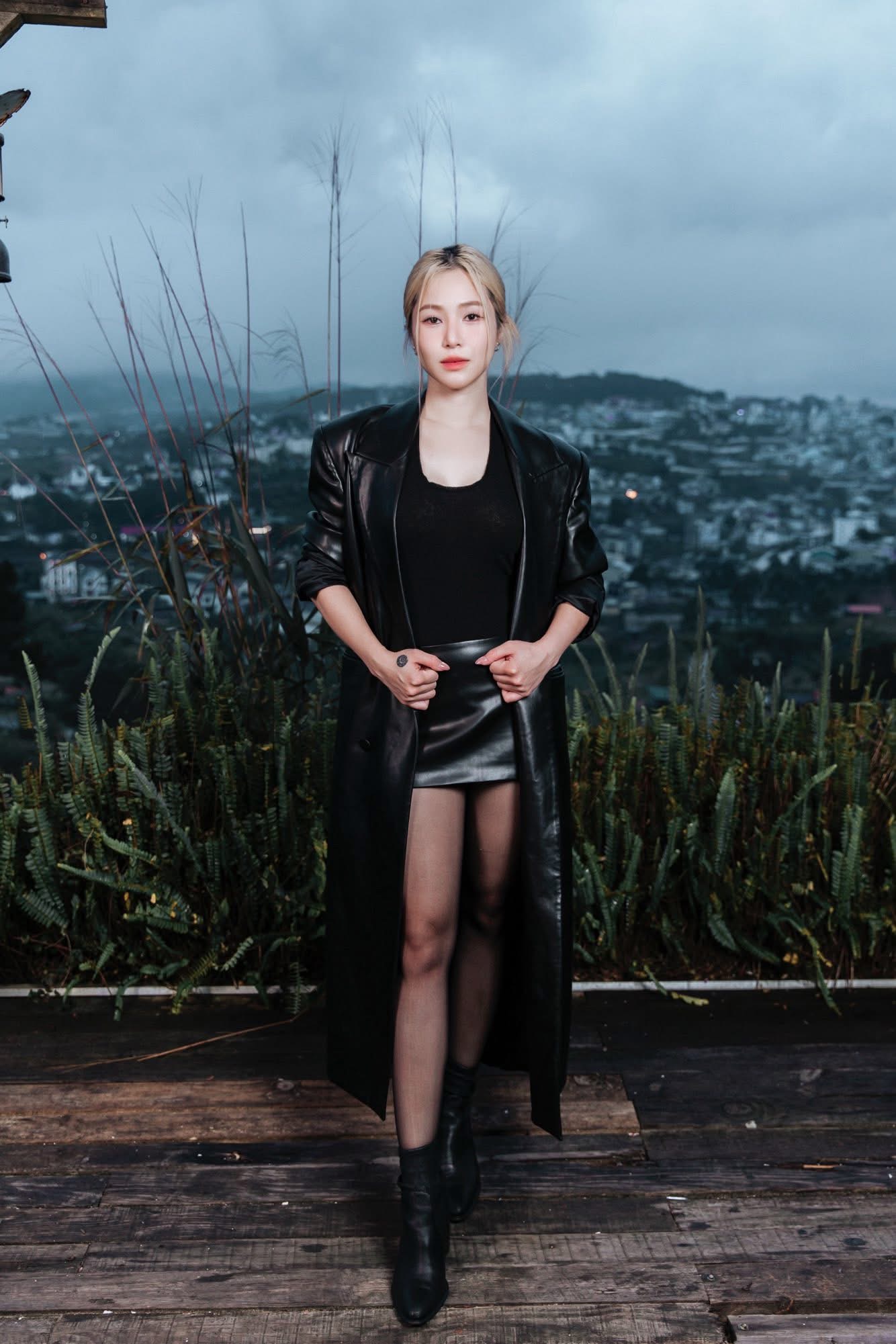 Đôi lúc Hương Tràm cũng Hương Tràm thể hiện phong cách thời trang cá tính, mạnh mẽ với tông đen toàn diện. Cô diện áo thun đen ôm sát kết hợp cùng chân váy da ngắn và áo khoác da dáng dài, tạo nên tổng thể vừa hiện đại vừa gợi cảm. Đôi boots cổ ngắn và tất mỏng giúp kéo dài đôi chân, mang đến vẻ ngoài phóng khoáng, tự tin.