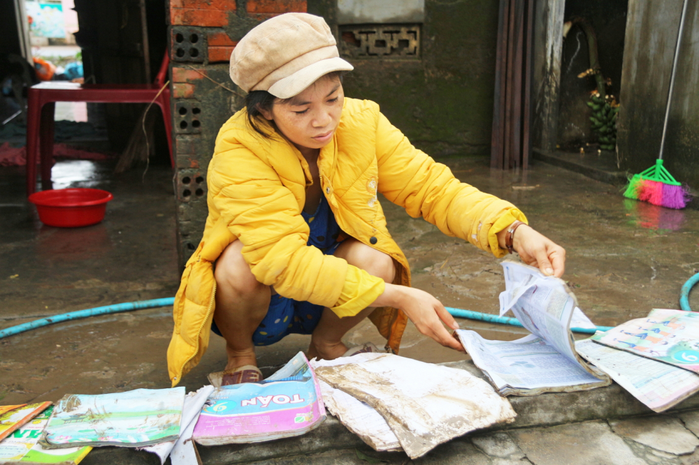 Chị Trương Thị Họa Mi xót xa khi chứng kiến đống sách vở của các con bị hư hỏng, lấm lem bùn đất ẢNH: NGUYÊN BẢO