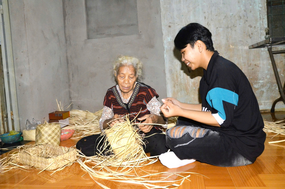 Bà Đào Thị Năm (xã Ngãi Giao) hướng dẫn nghề đan lát truyền thống của dân tộc Châu Ro cho cháu trai - ẢNH: TÙNG LÂM