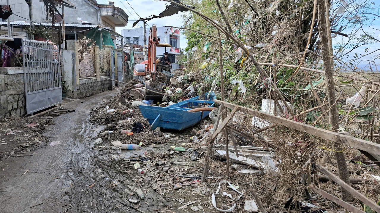 Từ sau lũ đến nay hơn 10 ngày, rác bao vây khu dân cư, ngập đường, phải dùng xe múc gạt rác qua một bên để xe máy chạy qua lại- Ảnh: Mạnh Trâm Trân 