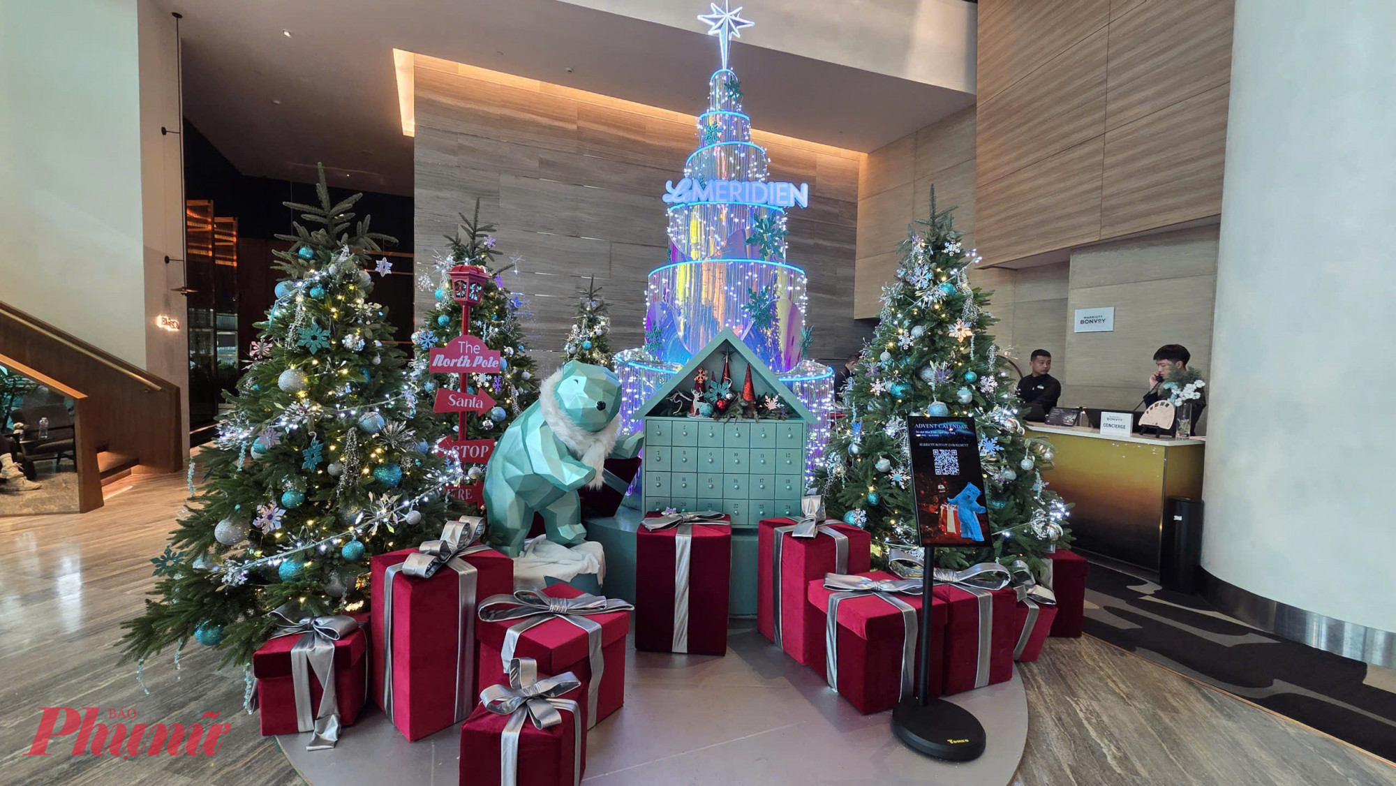 Tại khách sạn Le Meridien Saigon, không khí Giáng sinh được thổi bừng với phong cách trang trí hiện đại, rực rỡ ánh sáng và mang đậm dấu ấn trải nghiệm dành cho khách lưu trú. Ngay tại sảnh chính, cụm trang trí nổi bật với sắc xanh, bạc làm chủ đạo kết hợp những hộp quà đỏ kích cỡ lớn, cây thông phủ đầy đèn LED và biểu tượng mùa đông là chú gấu Bắc Cực.