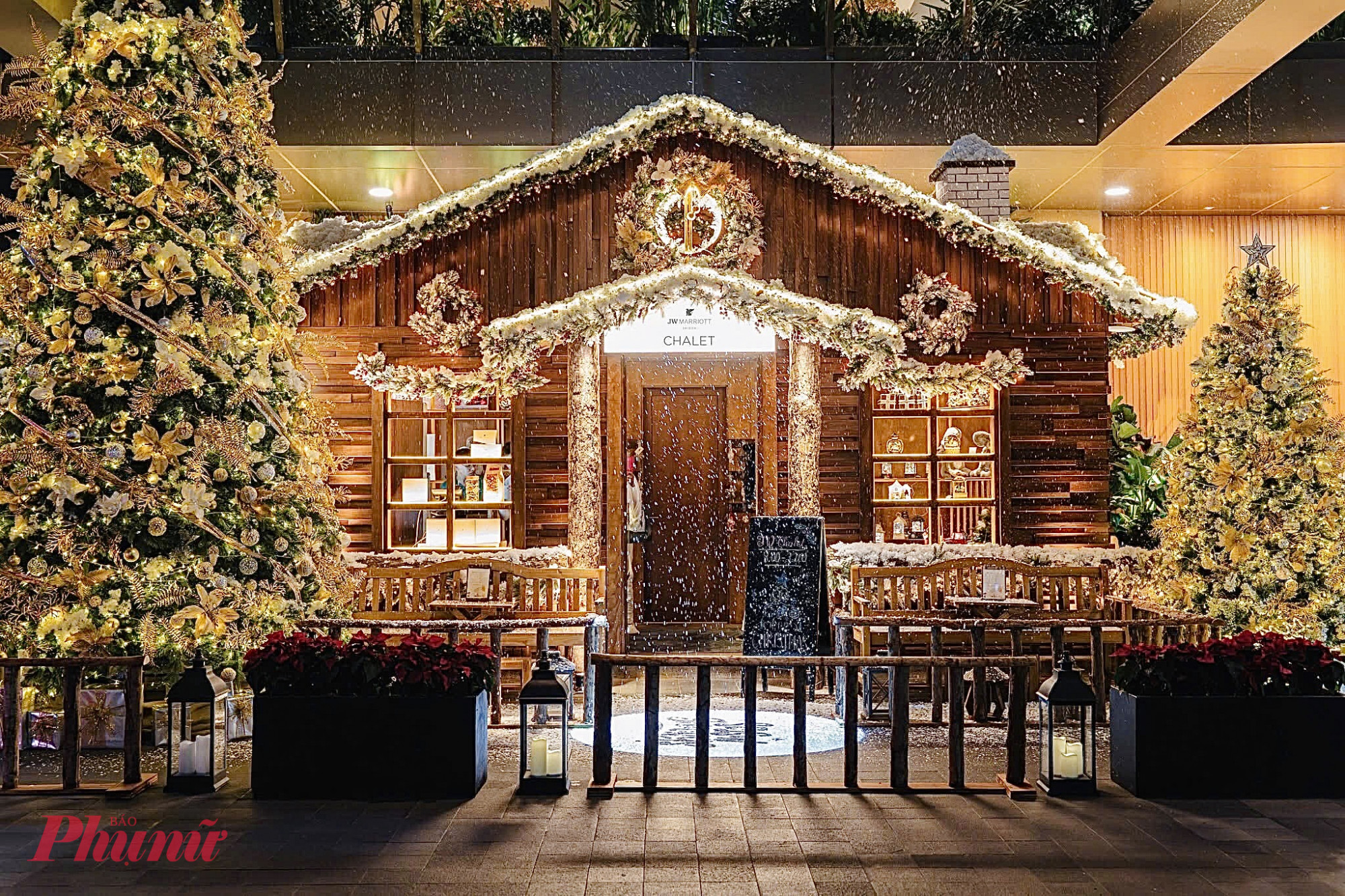 Điểm nhấn ấn tượng nhất là hiệu ứng tuyết rơi nhẹ ngay trước cửa chalet, tạo cảm giác như đang dạo bước giữa mùa đông thực thụ. Ánh sáng vàng ấm áp kết hợp cùng những chi tiết trang trí tinh xảo mang lại bầu không khí vừa lãng mạn vừa sang trọng, đúng tinh thần lễ hội cuối năm.