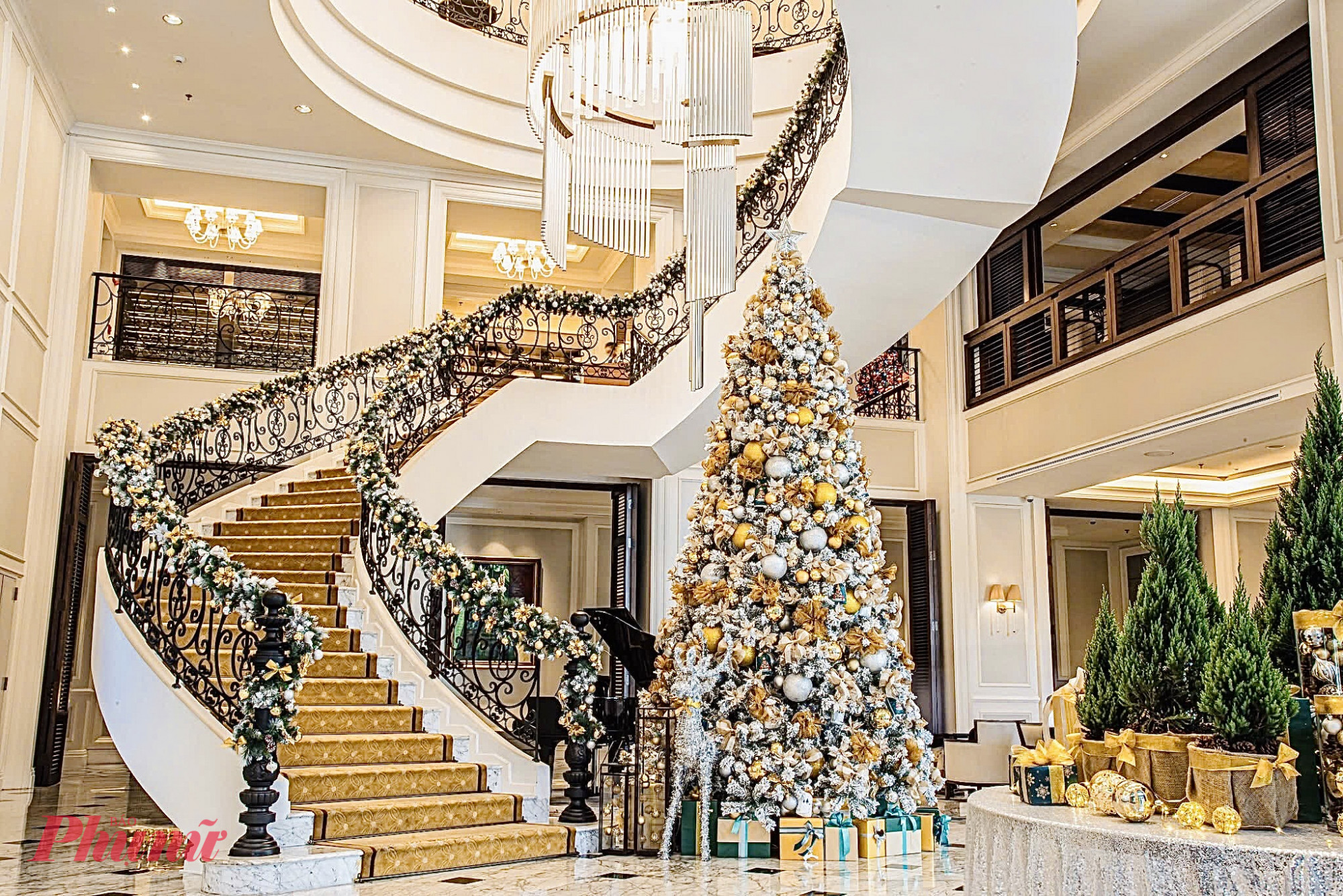 Không gian Giáng Sinh tại Mai House Saigon được trang trí theo phong cách sang trọng và tinh tế, mang đậm chất cổ điển châu Âu. Bảng màu vàng - trắng chủ đạo kết hợp với sắc xanh rêu của những cây thông tạo nên tổng thể hài hòa, vừa ấm áp vừa quý phái. Đại sảnh nổi bật với cây thông lớn phủ tuyết, được trang hoàng bằng những quả châu vàng bạc lấp lánh và những hộp quà sắc xanh - vàng được sắp đặt tinh tế dưới chân cây. 
