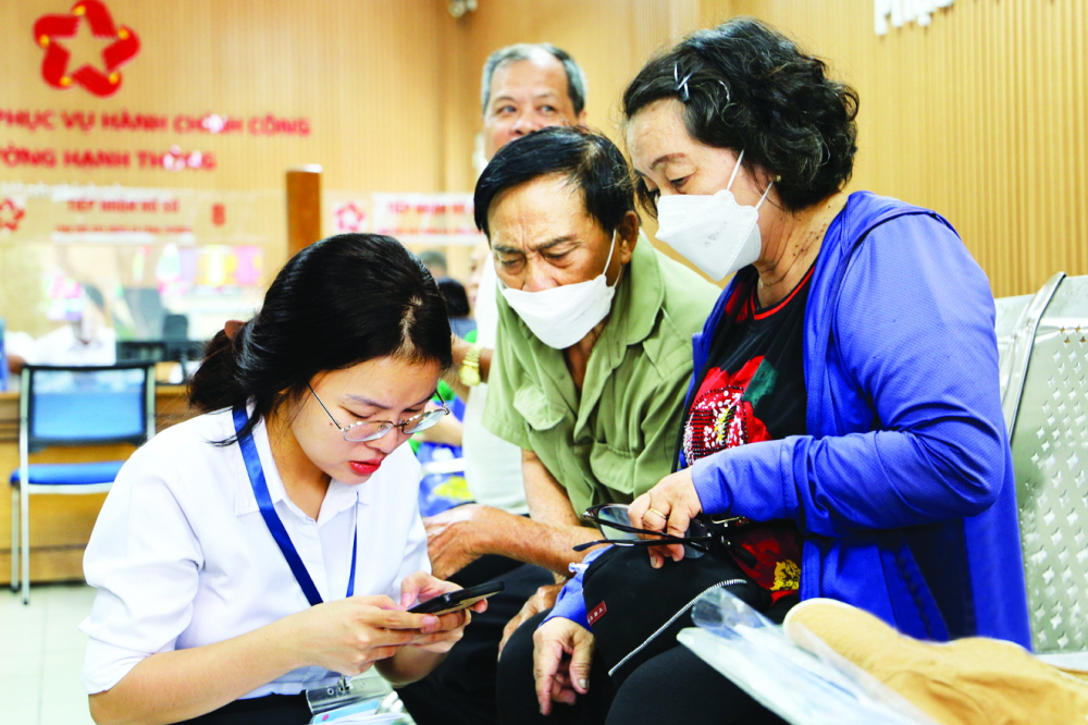 Cán bộ UBND phường Hạnh Thông (bìa trái) hướng dẫn người dân làm thủ tục hành chính qua các ứng dụng số