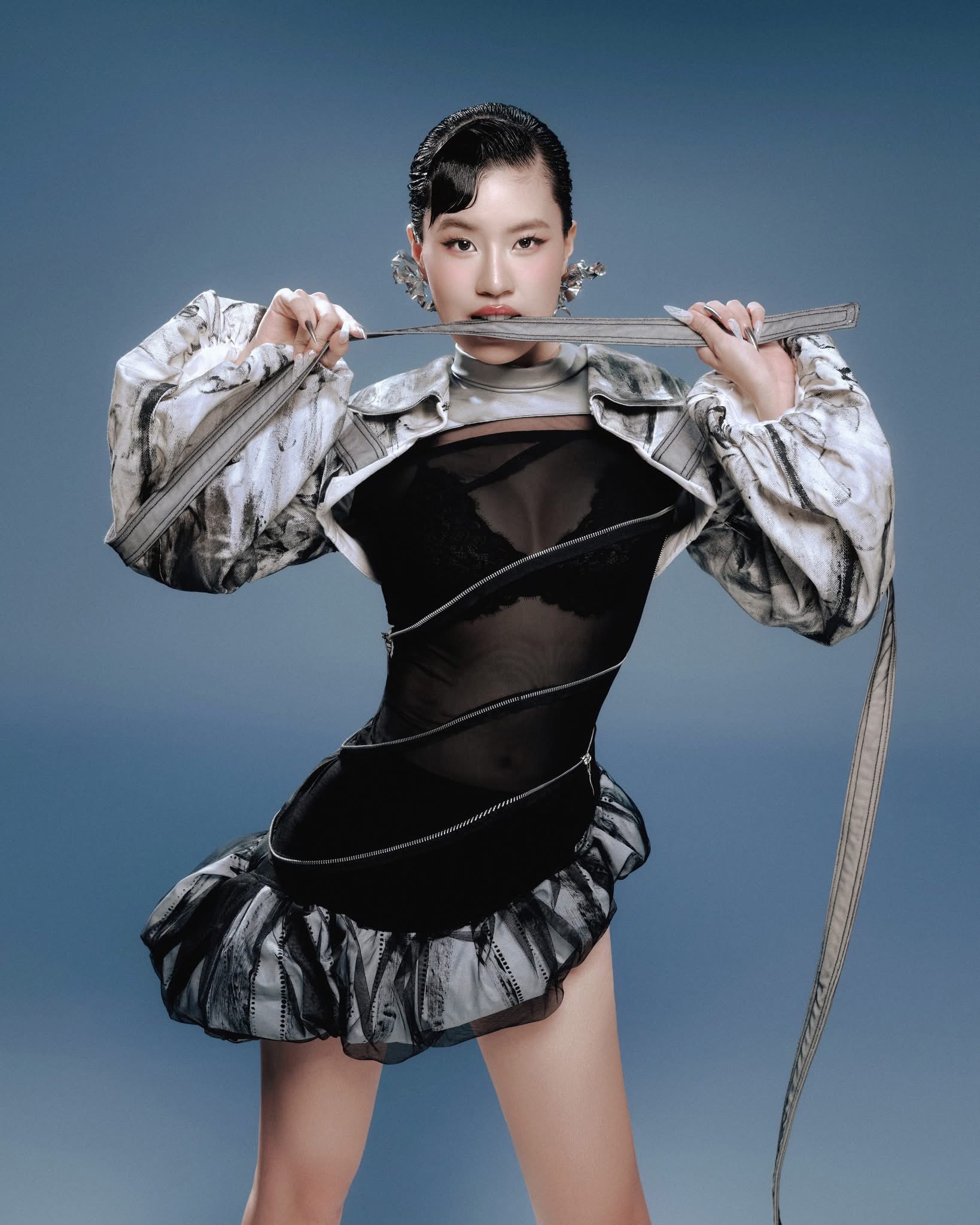 Pháo ghi điểm phong cách cuốn hút và thời thượng trong thiết kế váy đen xuyên thấu kết hợp đường zip uốn quanh cơ thể, tạo hiệu ứng thị giác mạnh. Áo khoác chất liệu ánh kim cùng hoa tai oversized mang đến vẻ cá tính, kiểu tóc vuốt gel và layout makeup sắc nét càng nhấn mạnh tinh thần bứt phá, sáng tạo trong hành trình làm mới bản thân của nữ rapper.