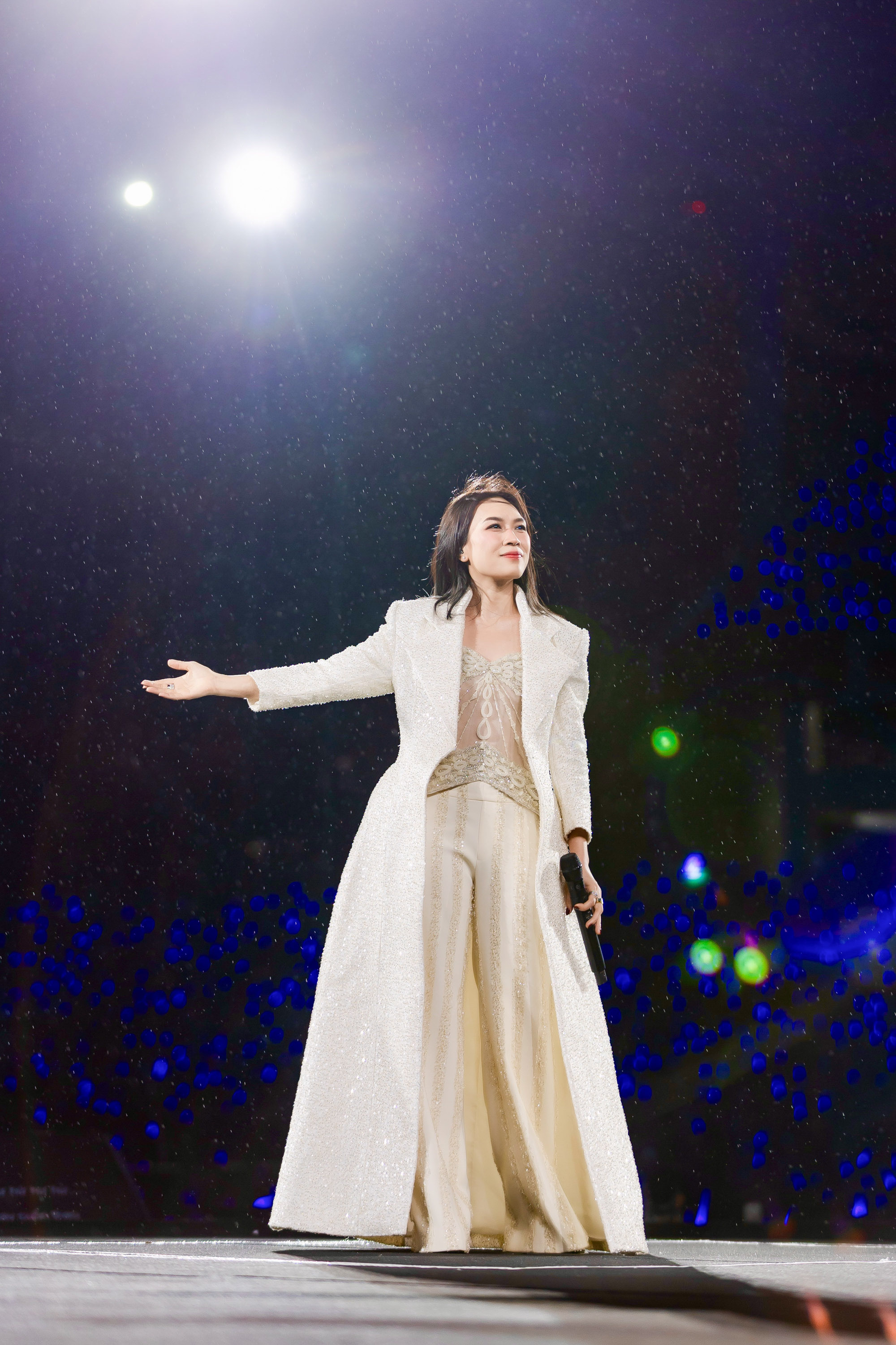 Mỹ Tâm lựa chọn tông trắng kem làm chủ đạo khi diện set đồ gồm áo corset xuyên thấu đính họa tiết tinh xảo kết hợp quần ống suông mềm mại, bên ngoài khoác áo choàng dài dáng phủ ánh kim nhẹ. Cách phối này tạo nên tổng thể vừa hiện đại vừa cổ điển. Thiết kế áo trong với chất liệu sheer giúp tổng thể thêm phần quyến rũ một cách tiết chế, trong khi phom dáng quần rộng mang lại sự thoải mái và khí chất phóng khoáng. 