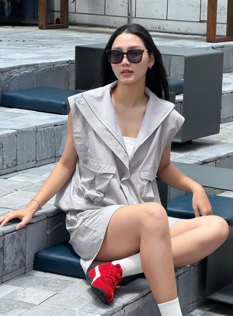 Nàng thơ mới của Trường Giang mang đến phong cách thể thao thời trang (athleisure) pha chút street style hiện đại. Set đồ tông trung tính với áo khoác sát nách phom rộng tạo cảm giác phóng khoáng, năng động nhưng vẫn giữ được nét thanh lịch. Cách phối cùng áo trong tối giản, kính râm và giày sneaker đỏ nổi bật giúp tổng thể thêm cá tính, trẻ trung. 