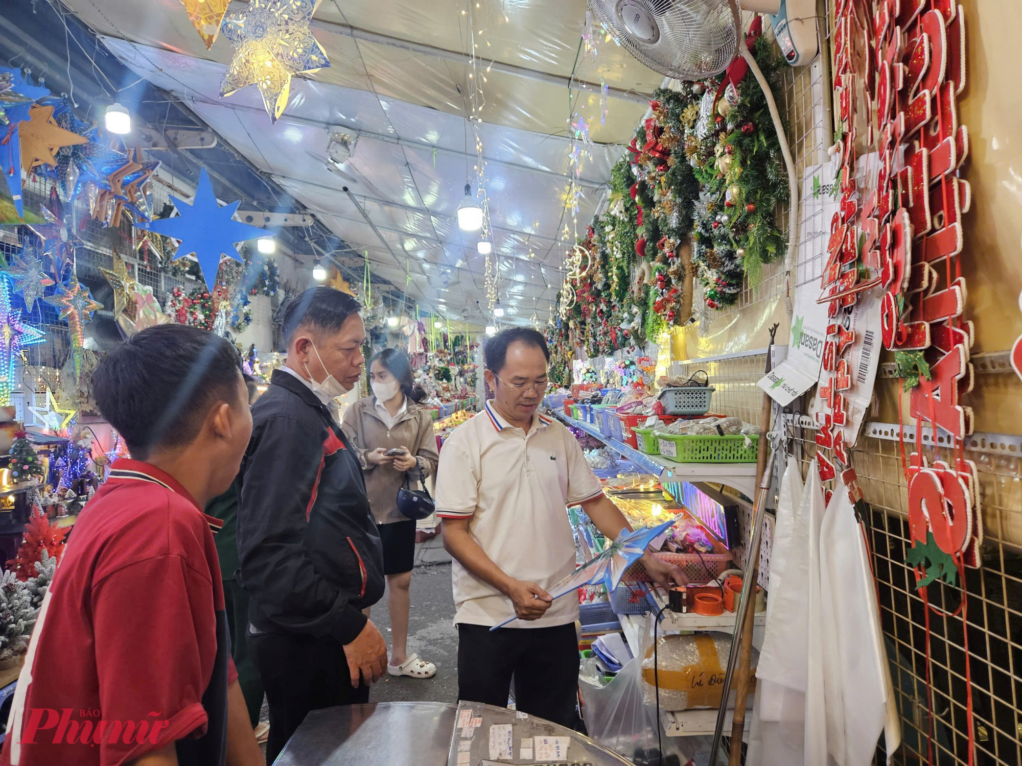 Theo ông Nguyễn Bảo Cường (áo trắng bên phải)- Quản lý cửa hàng đồ trang trí giáo xứ Tân Định, năm nay thị trường có nhiều mẫu mới, riêng mặt hàng cây thông có hơn 10 mẫu khác nhau. Tuy nhiên, sức mua giảm khoảng một nửa so với năm ngoái. Cũng theo ông Cường, giá bán năm nay cơ bản tương đương năm ngoái, không tăng. Cửa hàng bắt đầu bán từ đầu tháng 11, nhưng đến nay sức mua đã chững lại. 