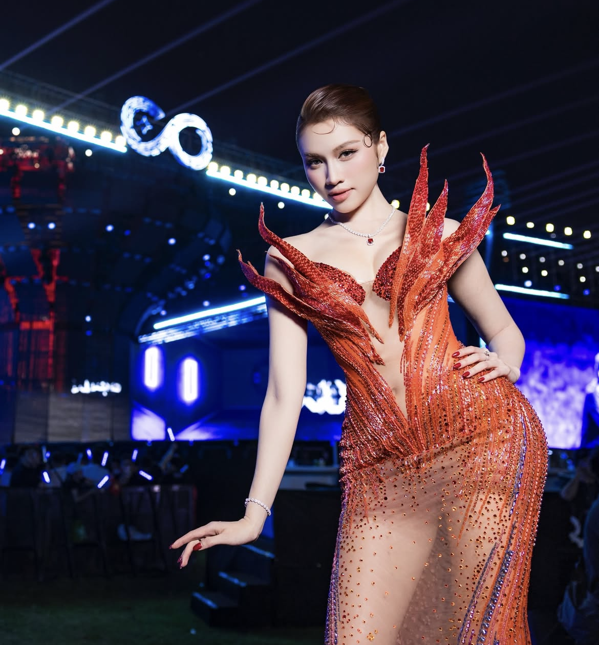 MC Thanh Thanh Huyền xuất hiện với bộ váy dạ hội mang tông đỏ cam rực, phom dáng ôm sát cơ thể với đường cắt xẻ sâu và các chi tiết dựng khối sắc cạnh ở phần thân trên. Thiết kế lựa chọn chất liệu xuyên thấu và cách xử lý bề mặt lấp lánh nhằm tạo hiệu ứng thị giác mạnh, tuy nhiên sự hở mức ở vùng ngực và thân váy khiến tổng thể trở nên phô trương. Các mảng dựng nhọn, thiếu tiết chế, kết hợp với độ hở cao làm mất đi sự tinh tế cần có của trang phục thảm đỏ, dễ tạo cảm giác kém duyên hơn là gợi cảm sang trọng. 