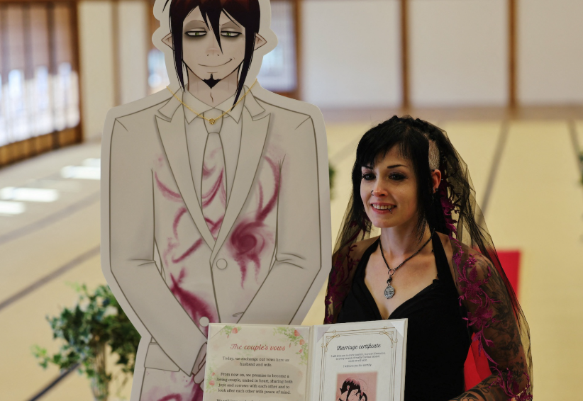 Một phụ nữ Úc 33 tuổi cầm giấy chứng nhận kết hôn bên cạnh bức tranh cắt của Mephisto Pheles, một nhân vật manga Nhật Bản mà cô nói rằng cô đang có mối quan hệ lãng mạn, trong đám cưới của họ tại nhà khách truyền thống Rinkokaku ở Maebashi, vào ngày 14 tháng 3.  Ảnh: REUTERS/Kim Kyung-Hoon